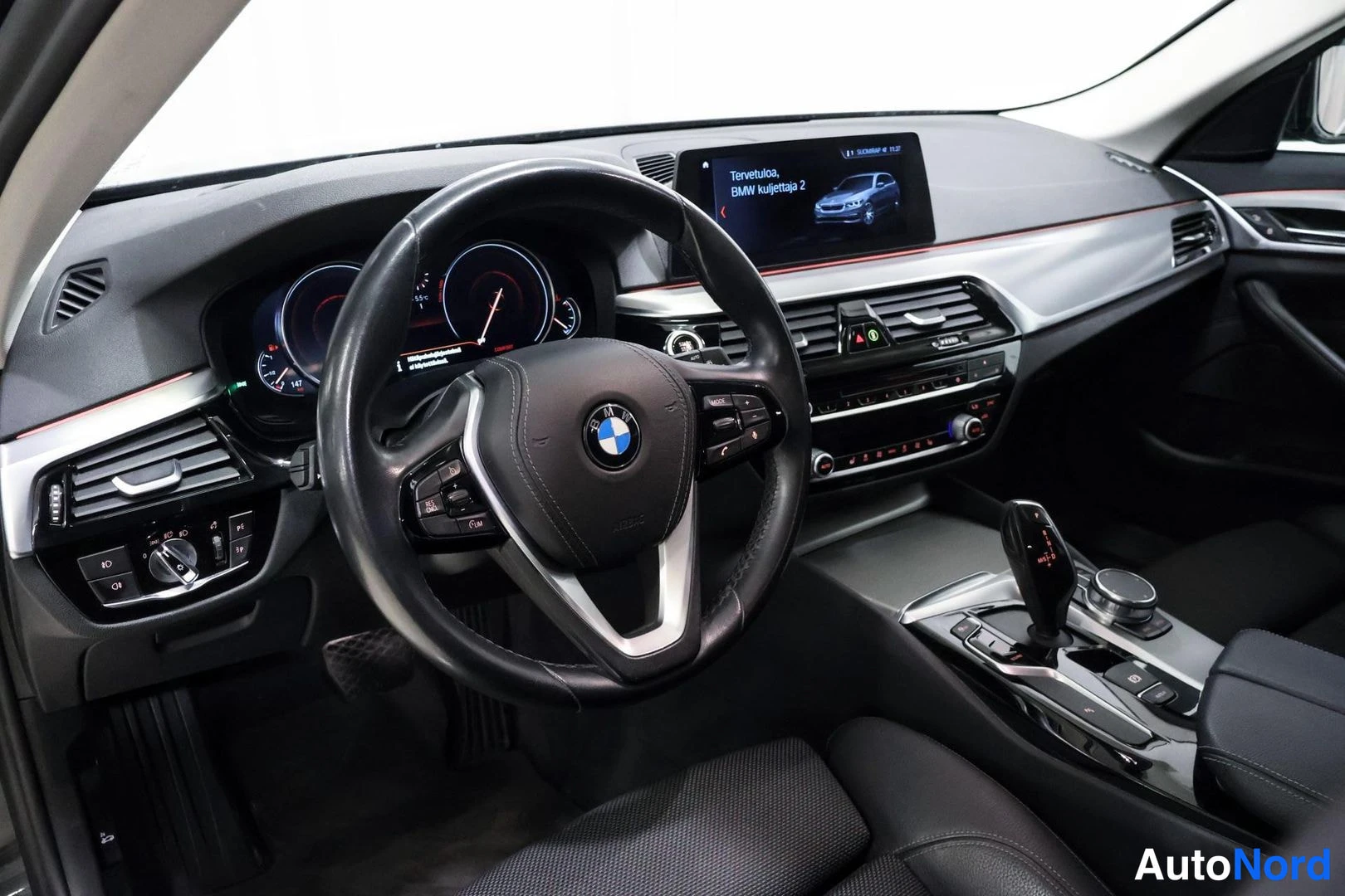 Muu: Ohjaamo vasemmalta: BMW-ratti, digitaalimittarit, keskitoiminnot ja näyttö, jossa teksti 'Tervetuloa, BMW kuljettaja 2'.