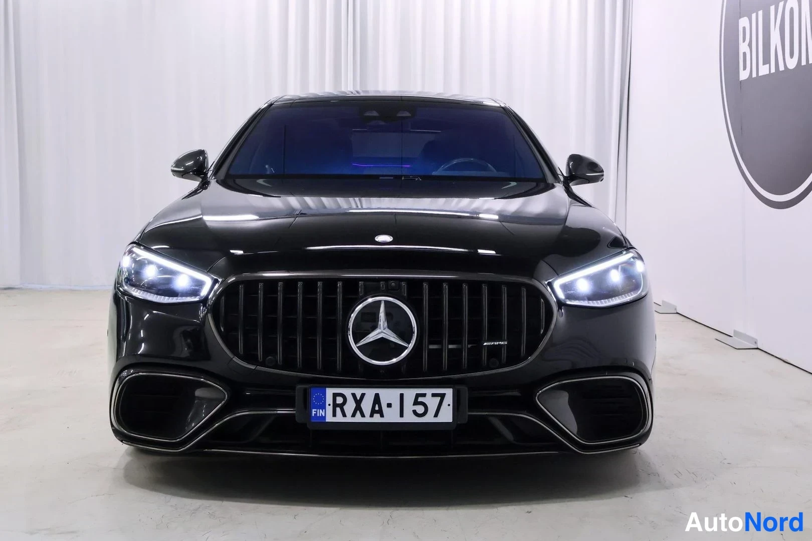 Edestä: Mustan Mercedes-sedanin etunäkymä, rekisteritunnus, panoraamikatto ja LED-ajovalot päällä.