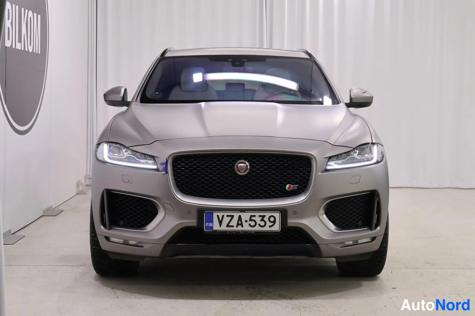 Edestä: Harmaanbeige Jaguar F-Pace suoraan edestäpäin, musta säleikkö ja rekisterikilpi.
