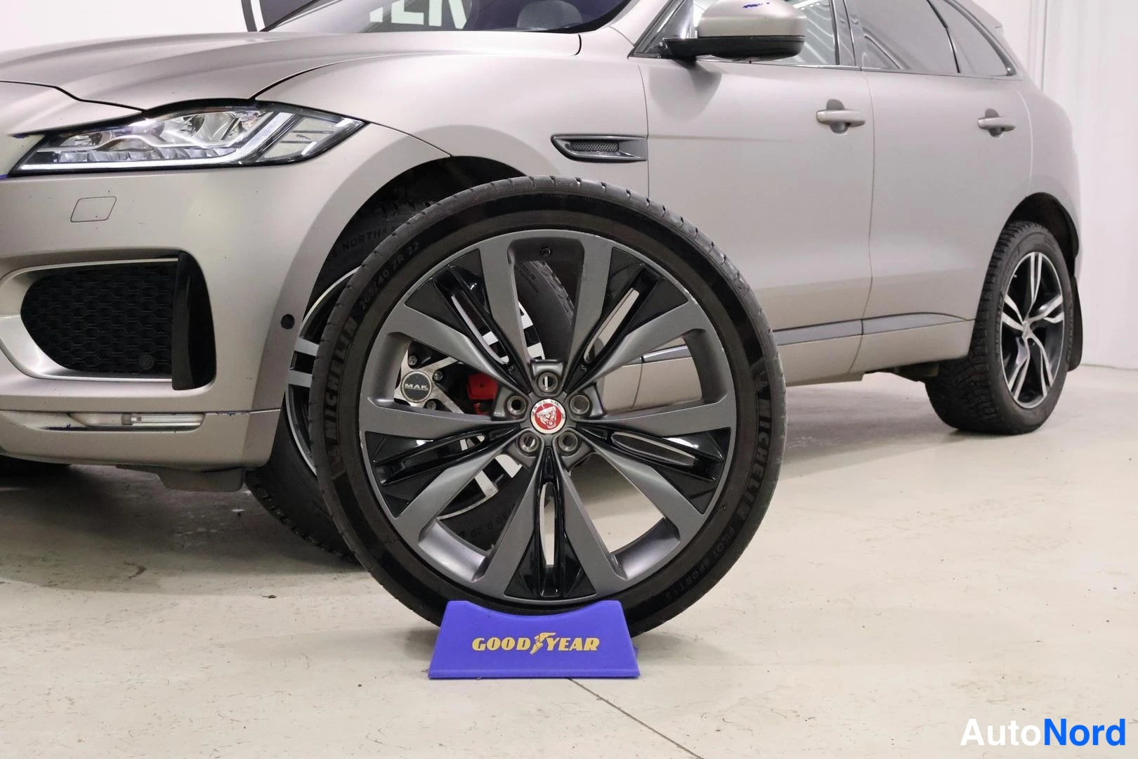 Etuviisto, nokka vasemmalle: Lähikuva harmaanbeige Jaguar F-Pacen etuosasta ja tummasta vanteesta, Goodyear-telineellä.