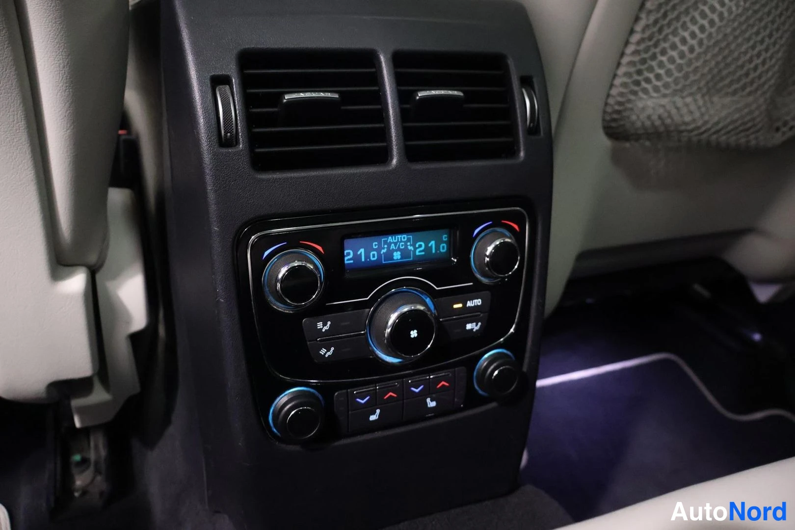 Yksityiskohta: Rear climate control panel located at the back of the center console. Features separate temperature displays set to 21.0 degrees Celsius for left and right side