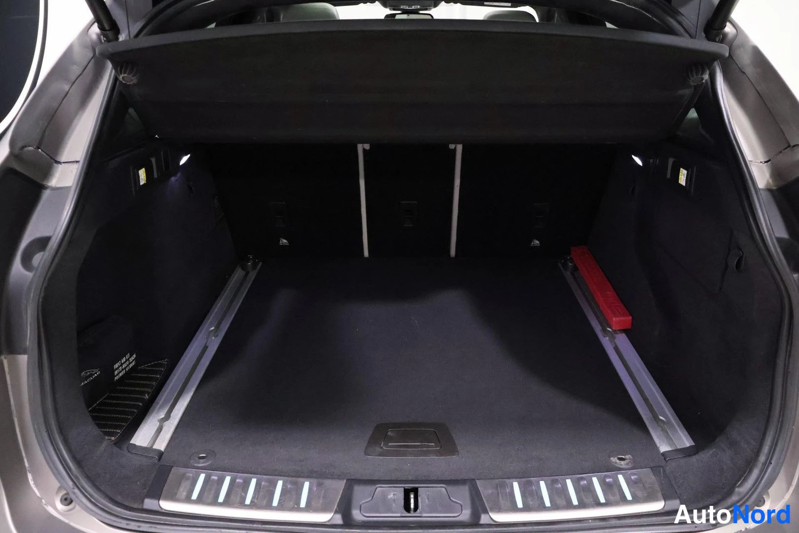 Tavaratila: Open cargo area of the trunk with the parcel shelf partially raised. The floor has a retractable cover removed, revealing tracks. Metal scuff plates are visible