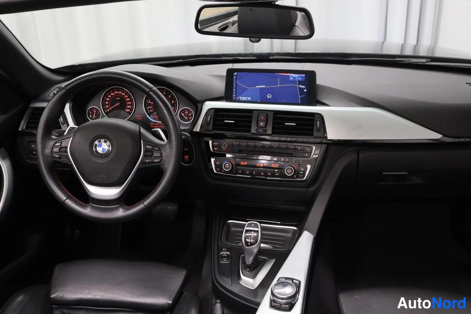 Muu: Sisätilakuva: musta kojelauta, BMW-tunnuksella varustettu ohjauspyörä, karttaa näyttävä keskinäyttö, automaattivaihteen valitsin ja ilmastoinnin säätimet keskik