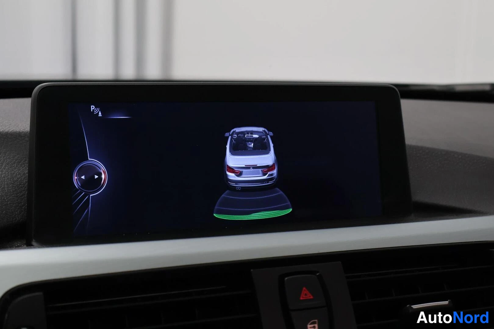 Yksityiskohta: Kojelaudan infotainment-näyttö näyttää pysäköintitunnistimen grafiikan: avoauton takaosan kuvan, vihreän anturikaaren ja P-symbolin anturiaalloissa.