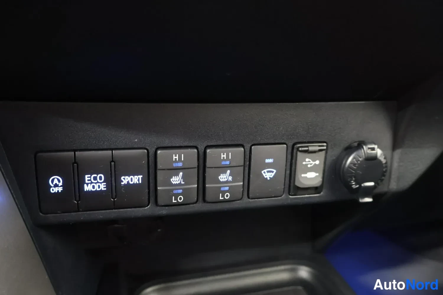 Yksityiskohta: Etumatkustajan puoleisen sivukonsolin paneeli: kytkimet ECO MODE, SPORT, HIT ja vasemman/oikean etuistuimen lämmitys, USB-liitin ja 12 V pesä.