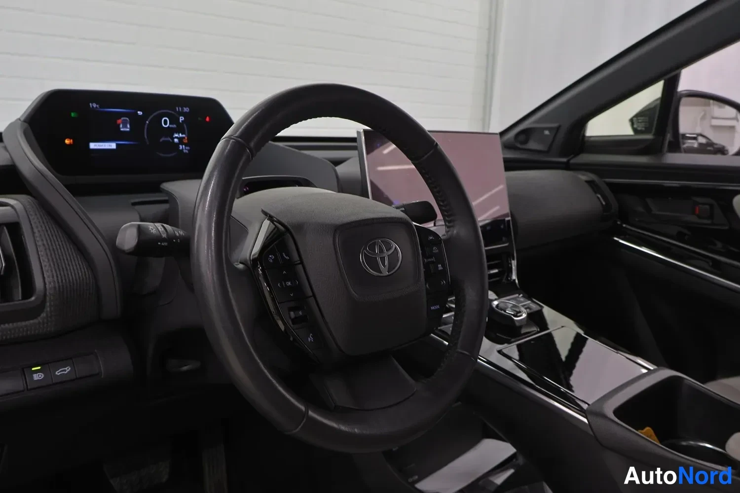 Yksityiskohta: Ohjaamon näkymä ohjauspyörään ja kojelaudan näytöille: Toyota-merkitty ohjauspyörä, pieni mittaritaulun näyttö ja suuri kosketusnäyttö keskellä.