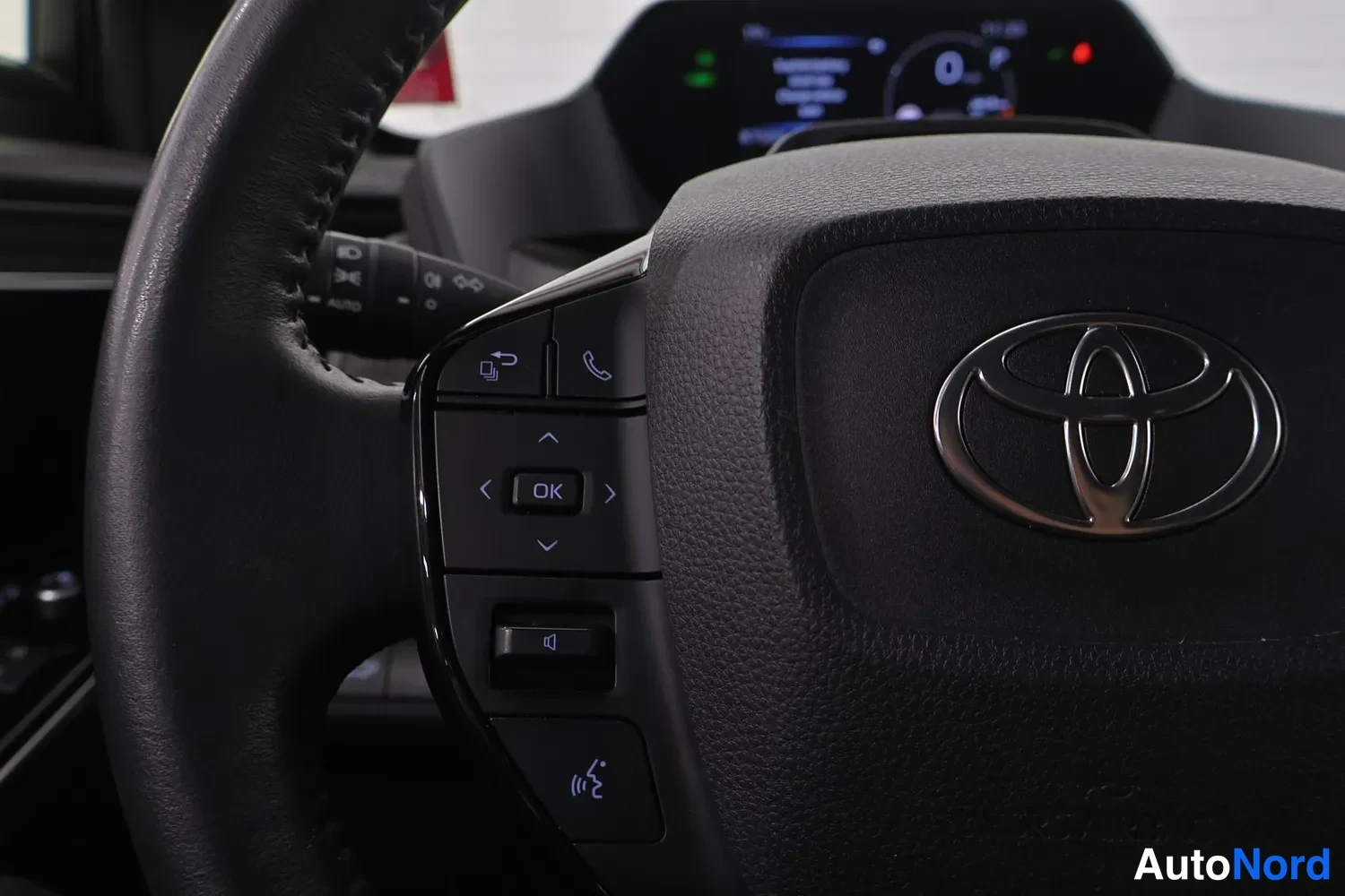 Edestä: Ohjauspyörän monitoimipainikkeet, Toyota-merkki ja digitaalinen mittaristo taustalla.