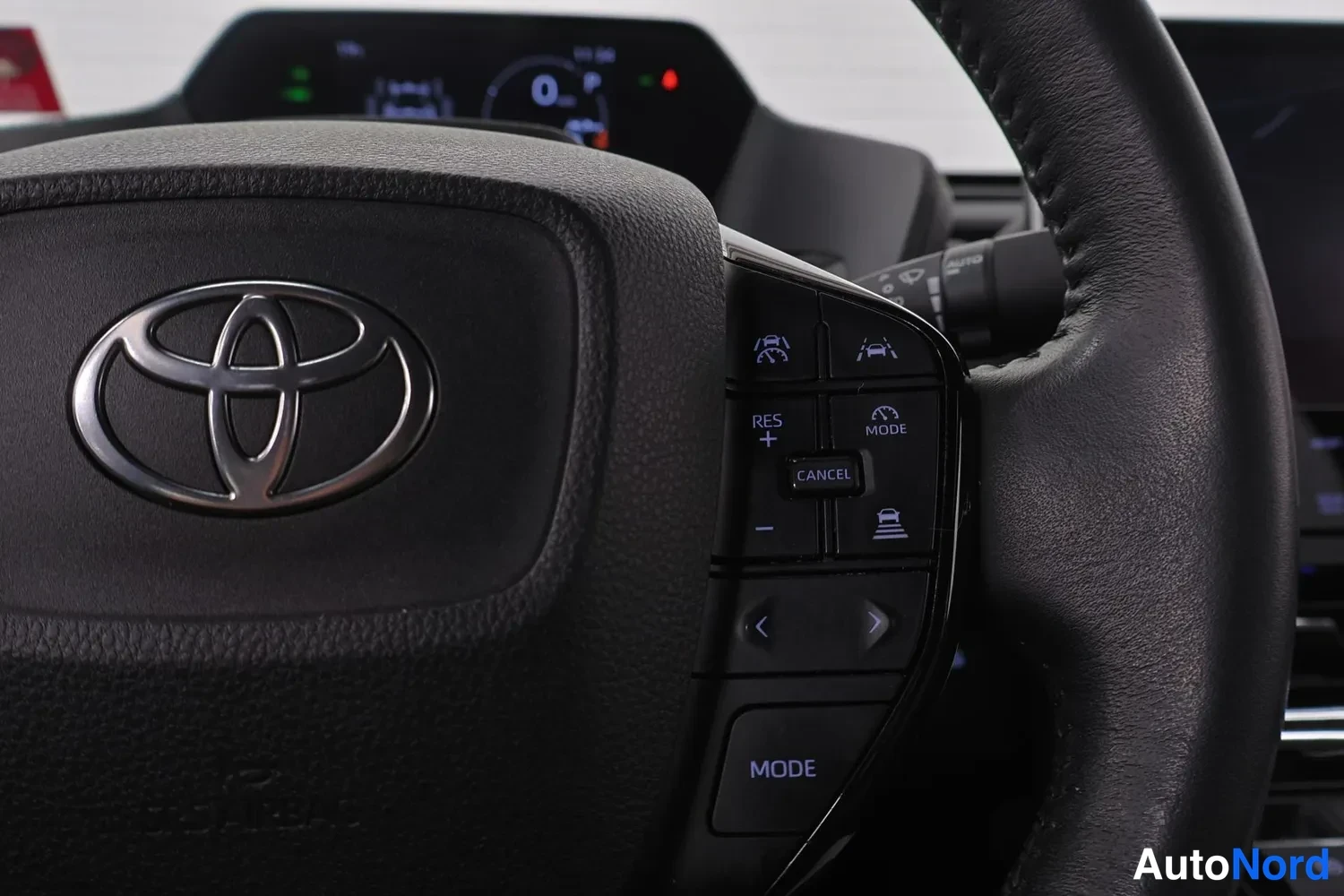 Sivulta: Lähikuva mustasta Toyota-ohjauspyörästä: ilmatyynyn kannessa Toyota-logo, oikealla kytkimellä RES+, CANCEL ja MODE -napit sekä etäisyys- ja kaistapitoikoneja, t