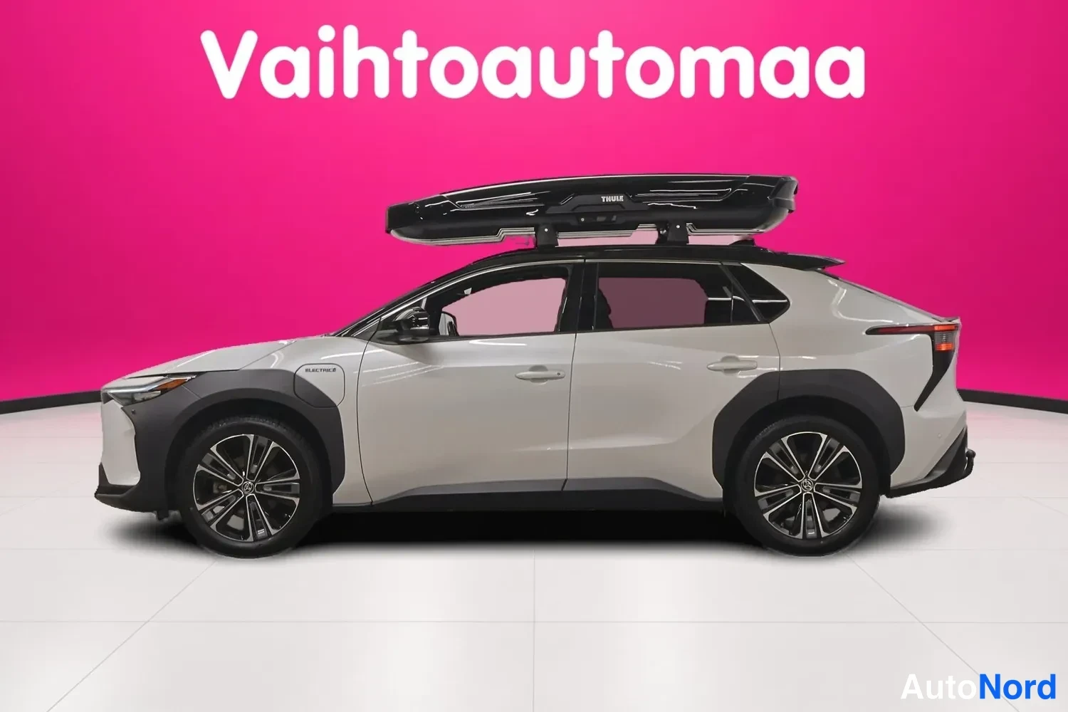 Sivulta: Toyota bZ4X, valkoinen, kylki vasemmalta, Thule-kattolekella, tausta vaaleanpunainen studio.