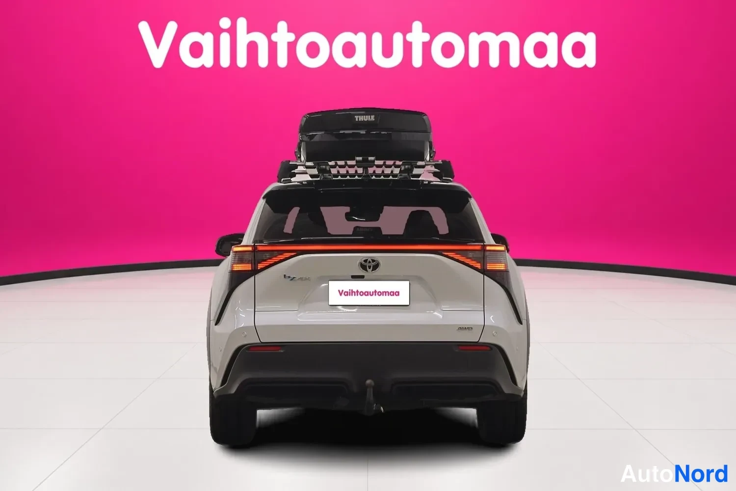 Takaa: Auton takaosa suoraan takaa: poikittainen takavalojen palkki, Toyota-merkki, musta Thule-kattoboksi ja vetokoulu näkyvissä.