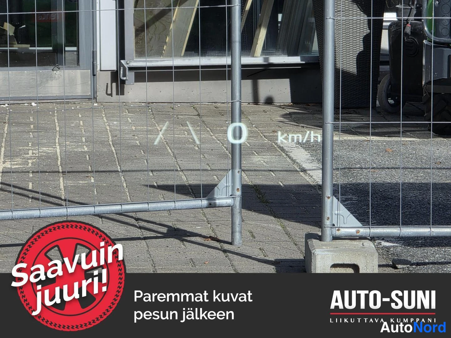 Muu: Kuva autopaikasta rakennusaidan takana, teksti '0 km/h' kuvan keskellä,Auto-Suni-logo ja teksti 'Saavuin juuri! Paremmat kuvat pesun jälkeen'.