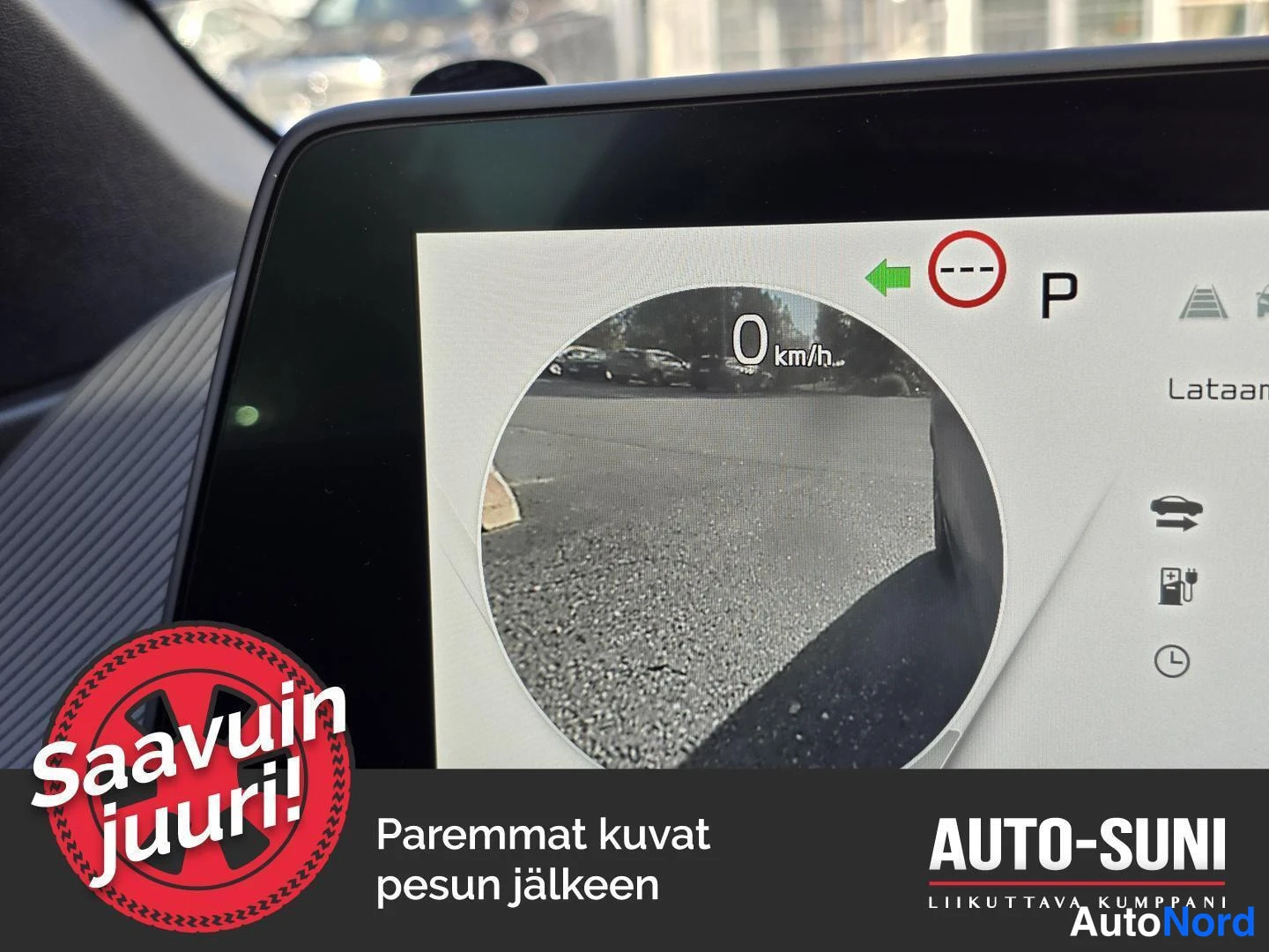 Muu: Autoon liitetyn näytön takakamera kuva; näytössä nopeus 0 km/h, P-merkki ja teksti 'Lataan'.