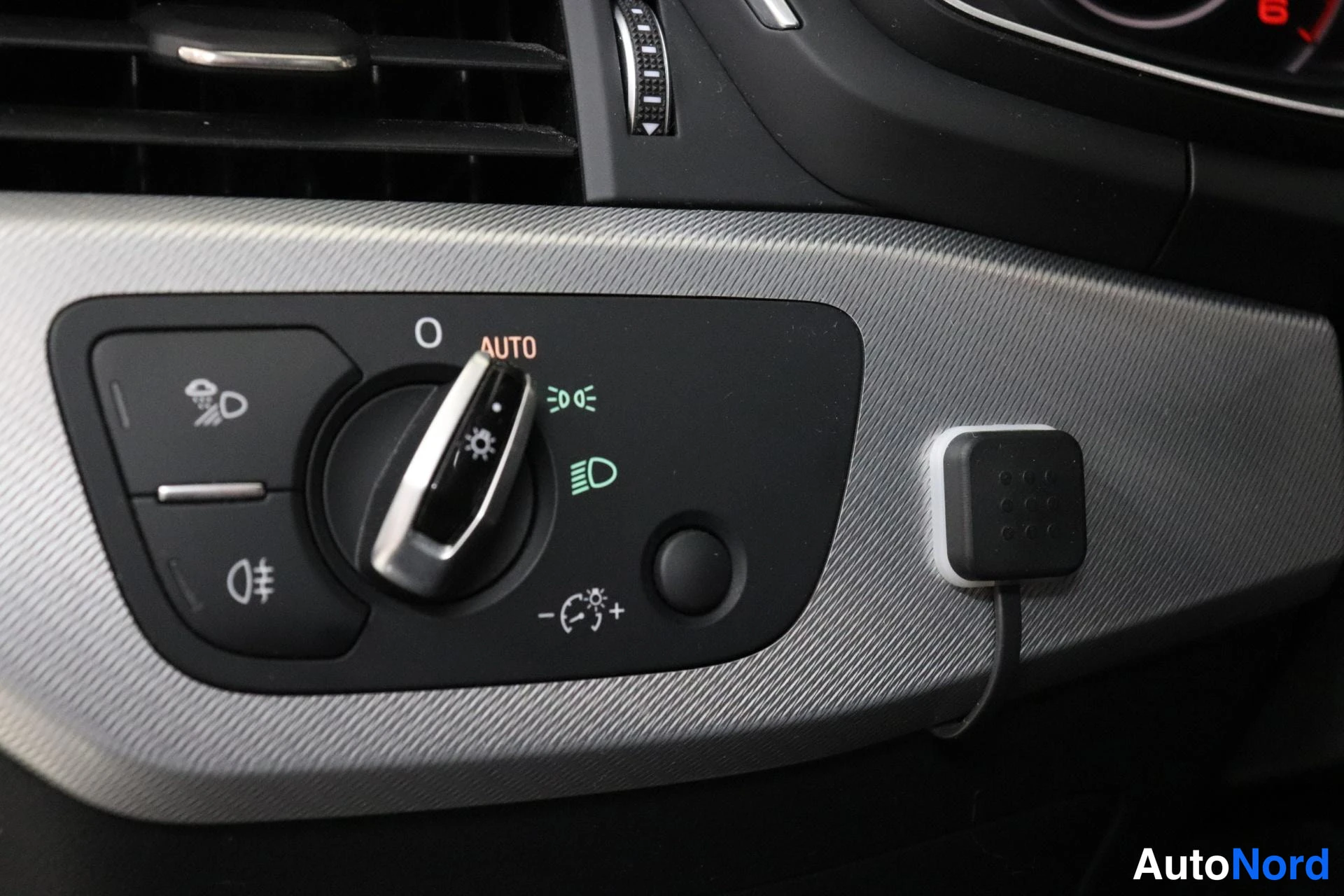 Yksityiskohta: Valaistuksen ohjausnuppi kojelaudassa: AUTO-asento, sumuvalojen merkit, lyhyt- ja pitkien valojen symbolit sekä valonkorjaimen säätöruuvi.