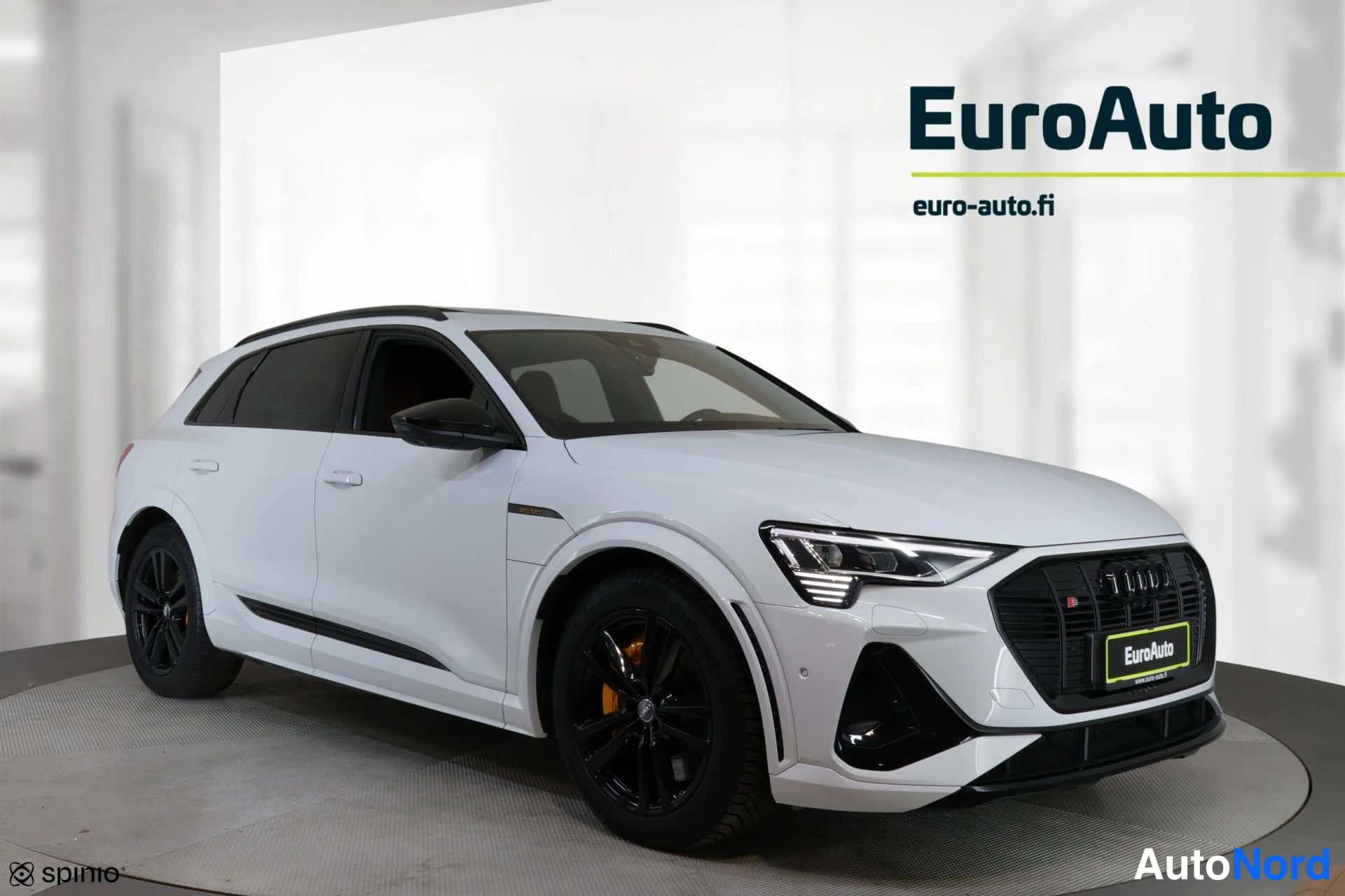 Etuviisto, nokka oikealle: Valkoinen Audi e-tron etukolmanneskuvassa, keula kuvan oikealla laidalla; musta etusäleikkö, mustat vanteet ja kattokaiteet.