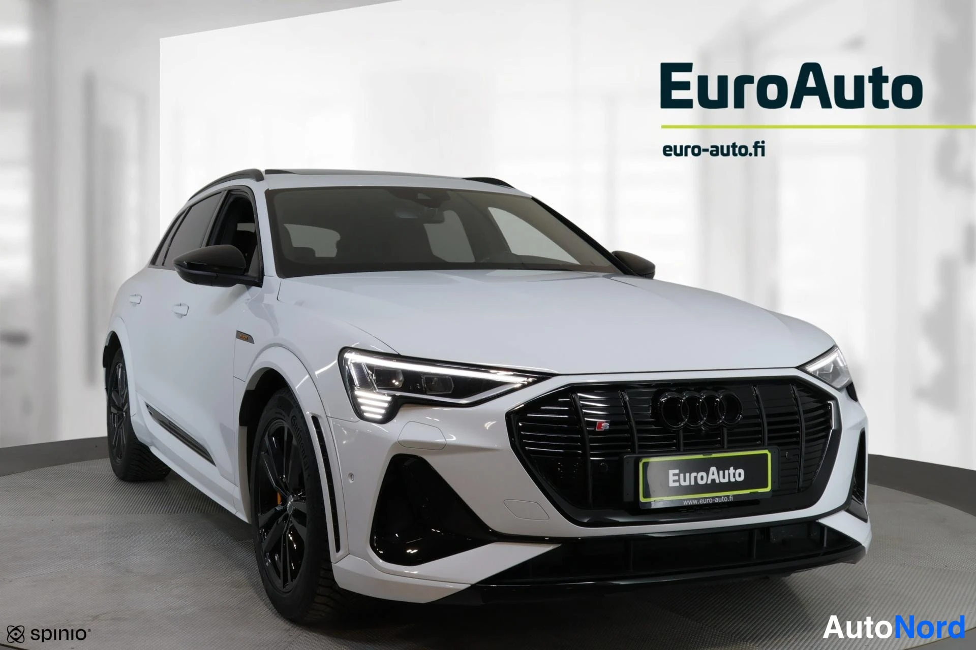 Etuviisto, nokka oikealle: Valkoinen Audi e-tron kuvattuna lähes suoraan edestä keula hieman oikealla; musta etusäleikkö, mustat vanteet ja kattokaiteet.
