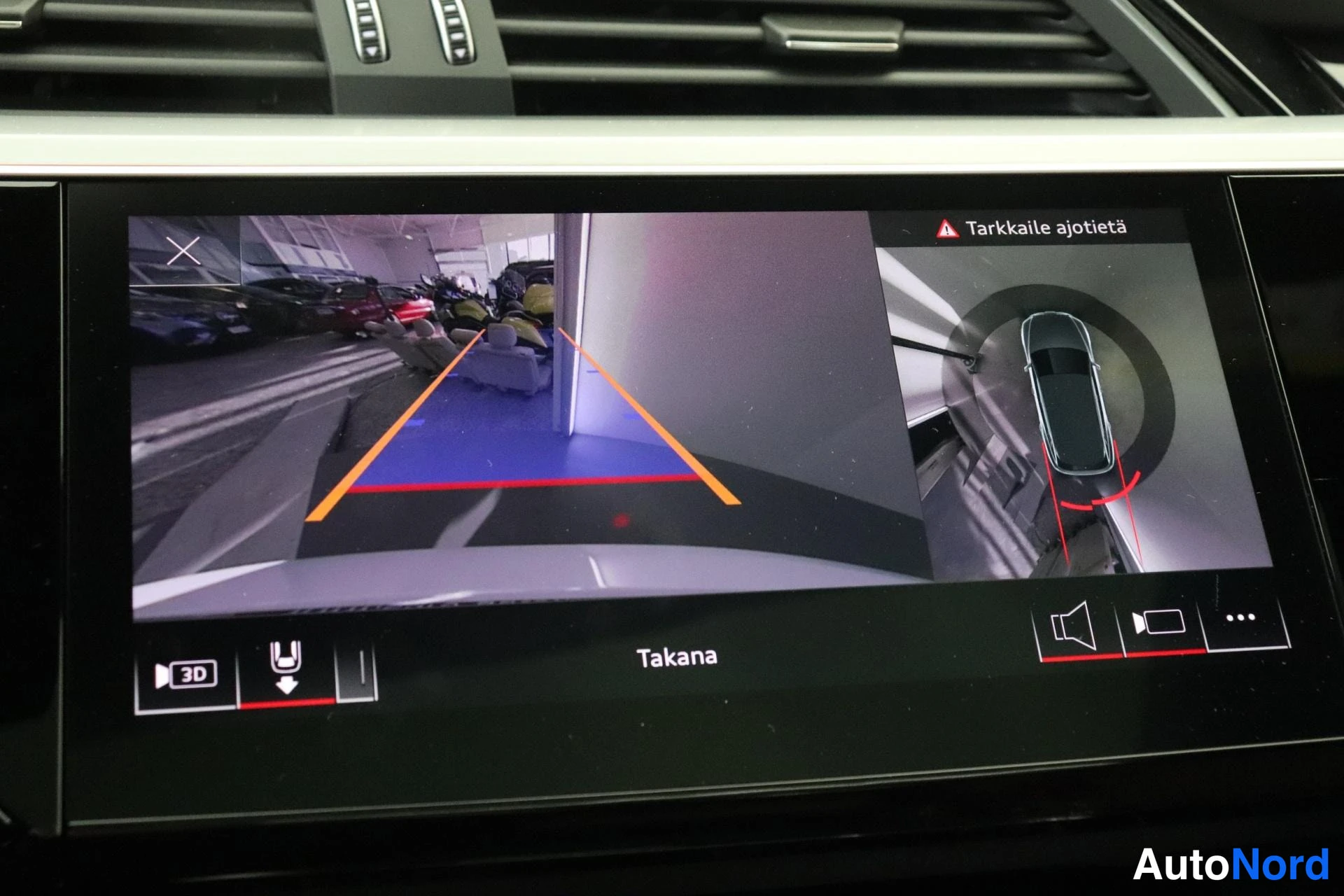 Edestä: Keskikonsolin näyttö: peruutuskameran kuva opastusviivoilla ja 3D-ylänäkymä autosta, teksti 'Takana' ja varoitus 'Tarkkaile ajotietä'.