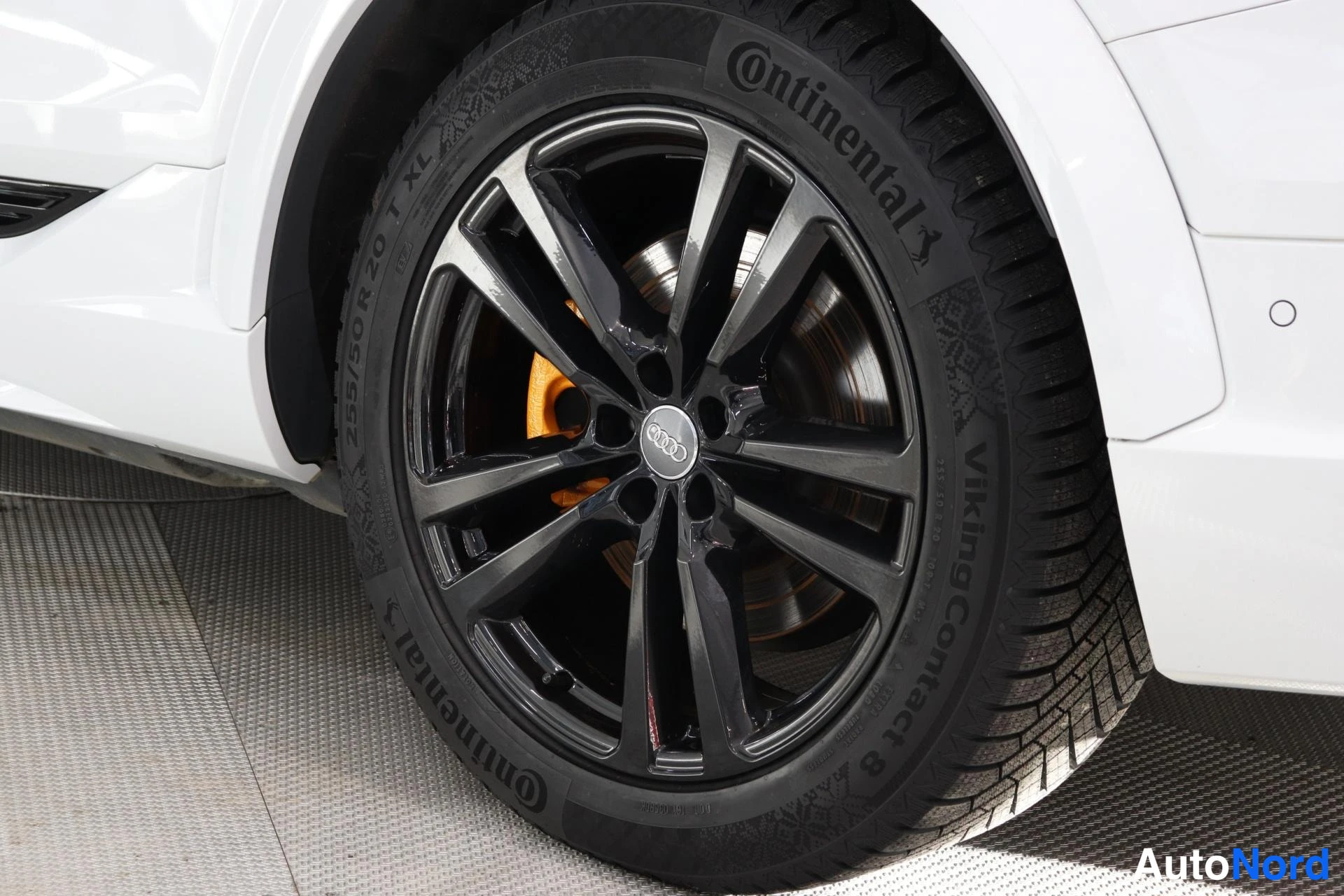 Sivulta: Lähikuva auton pyörästä: musta vanteen keskiö Audi-logolla, Continental VikingContact 8 -rengas, jonka sivuseinässä lukee 255/50 R 20 XL; valkoista koria näkyy