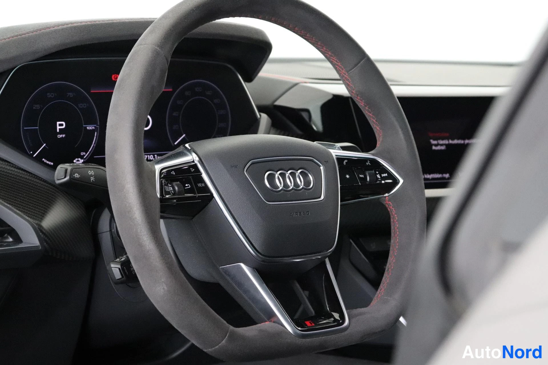 Ohjaamo: Ohjauspyörä Audi-logolla, punainen ommel, takana digitaalinen mittaristo näytöllä jossa P-valinta