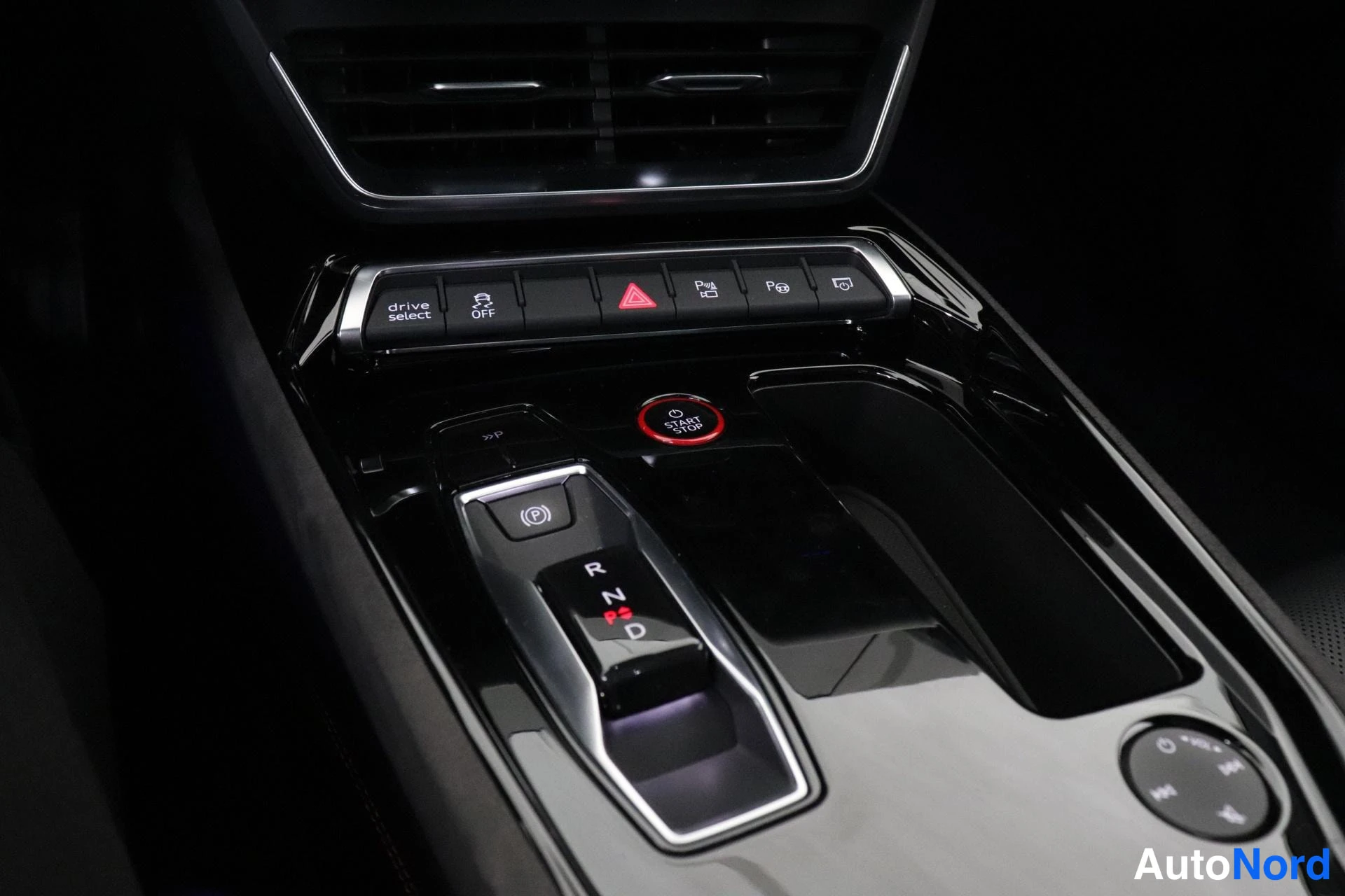 Yksityiskohta: Keskikonsolin vaihteenvalitsin, jonka merkit R, N, P ja D näkyvät, punainen start/stop-painike sekä drive select -painikerivi console-tyylisellä kiiltävällä pan