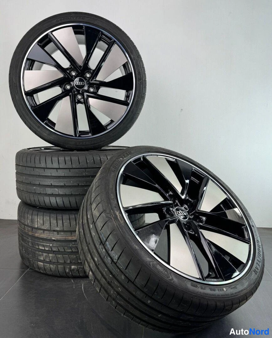 Yksityiskohta: Neljä mustaa Audi-alumiinvanne–rengas-paria päällekkäin; vanteissa kiiltävät ja hiotut pinnat, rengassivuseinässä Goodyear-teksti.