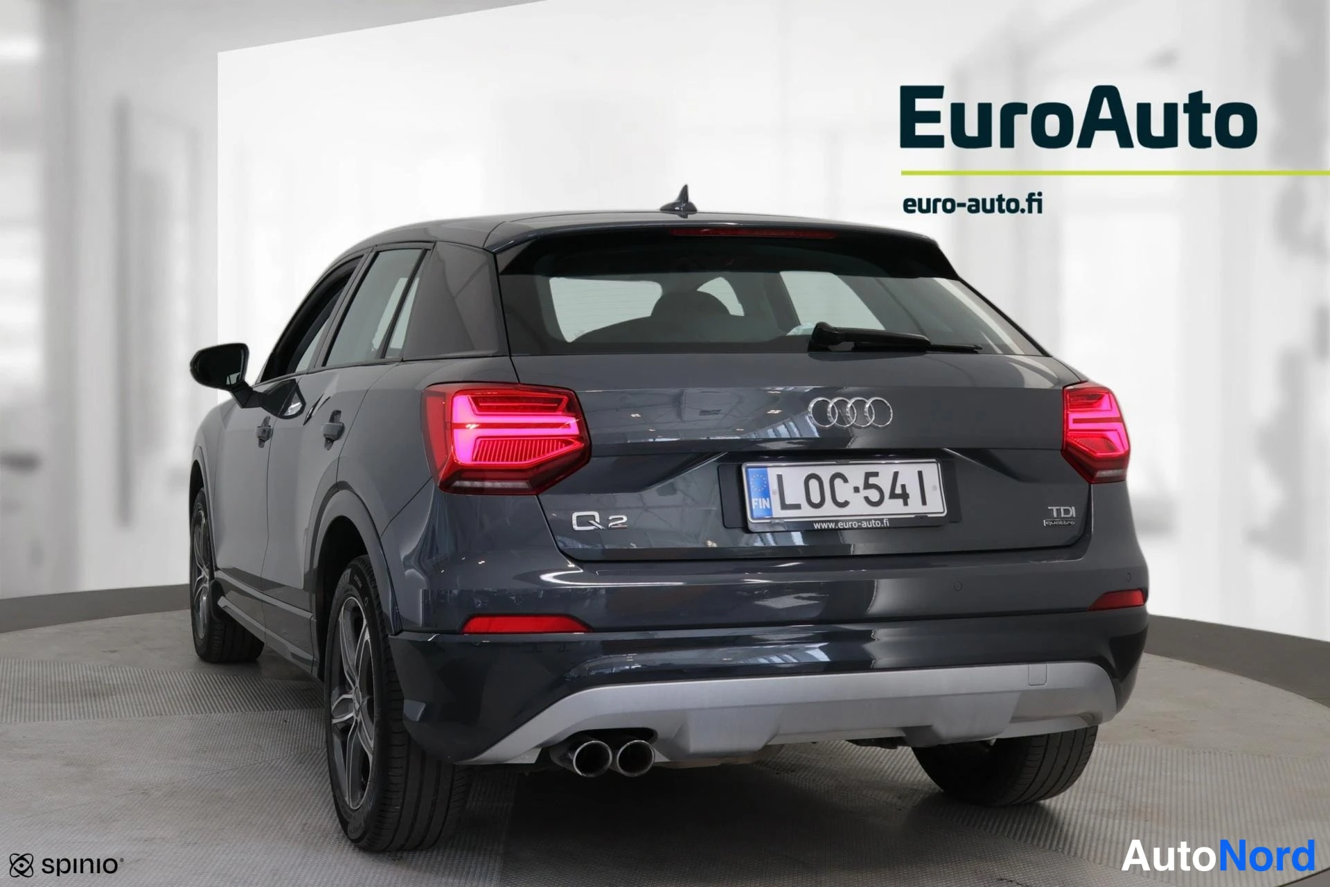 Takaviisto: A dark grey Audi Q2 parked in a studio with its rear and the left flank visible. The license plate and TDI badge are clearly seen.