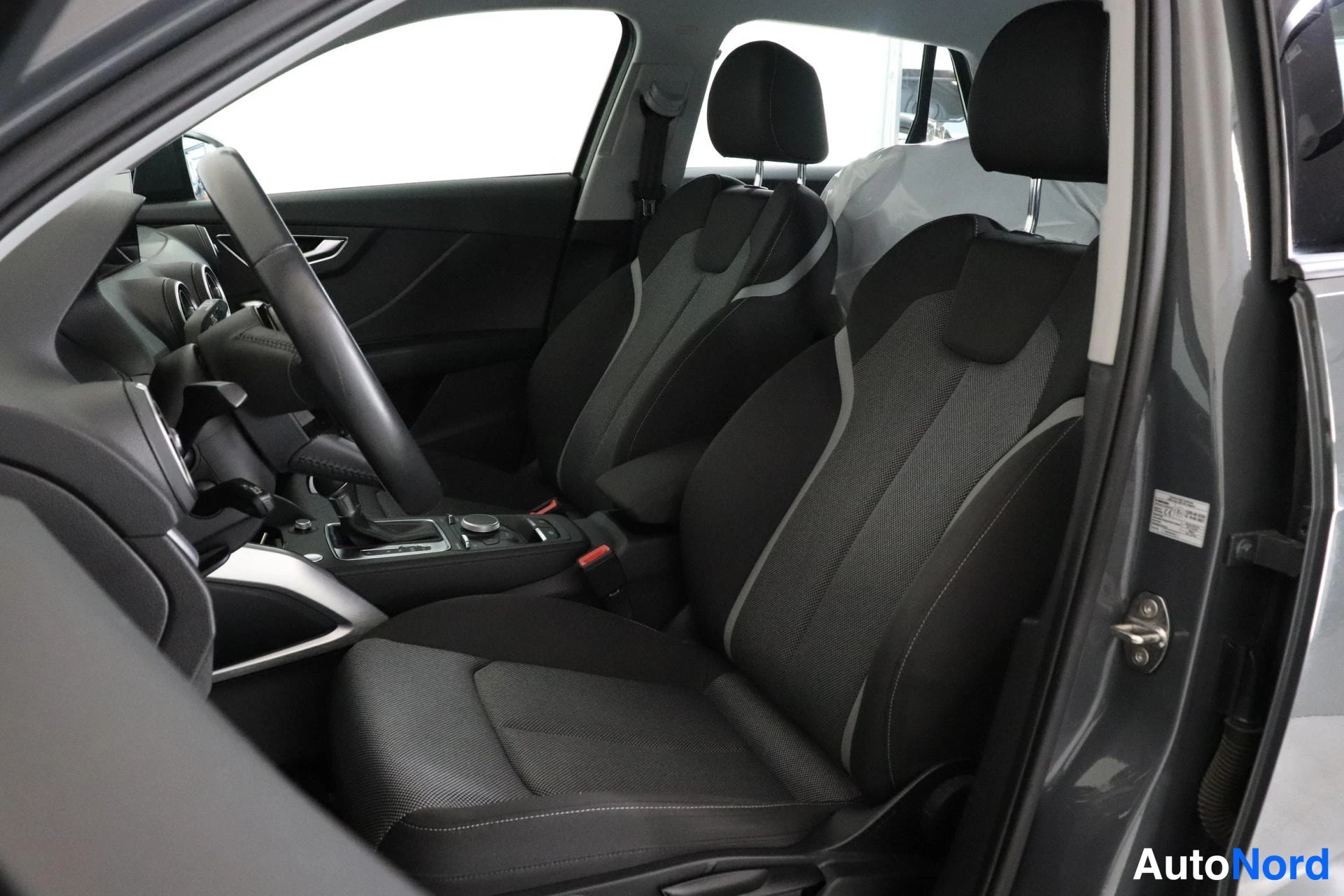 Etuistuimet: The front seats upholstered in black fabric with silver piping are shown from the open passenger door perspective.