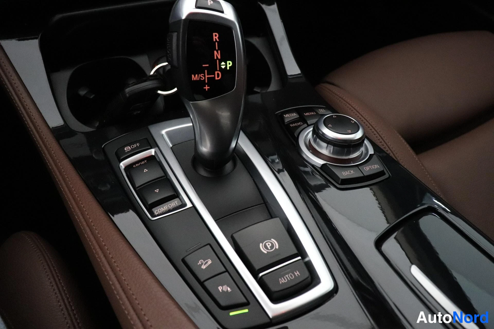 Yksityiskohta: Center console featuring automatic gear selector in P position with illuminated display, iDrive control knob to the right, drive mode selector (Comfort/Eco Pro)