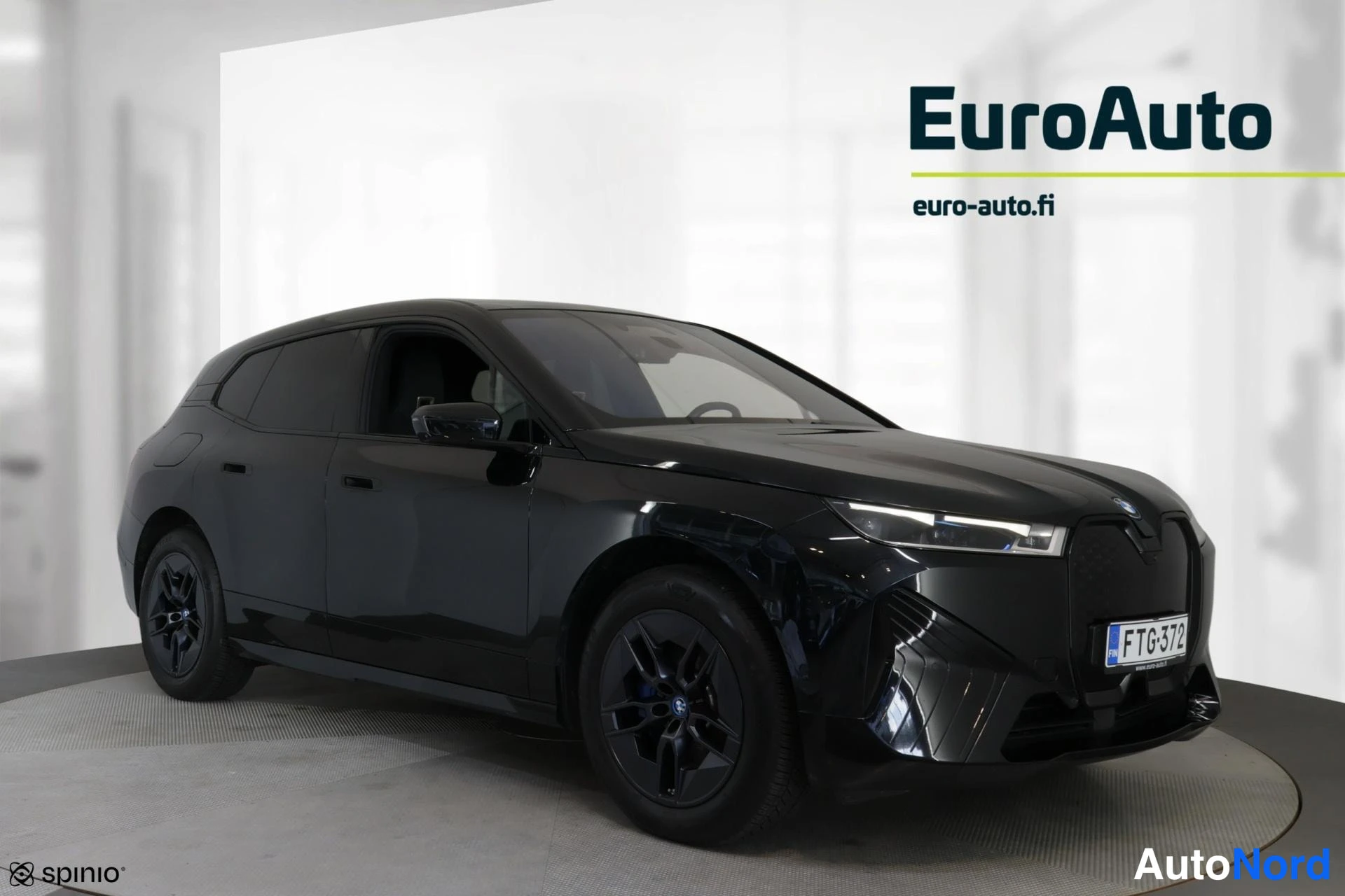 Etuviisto, nokka vasemmalle: Kuvan oikea etu kolminkertainen näkymä. Tummanharmaa BMW-iX on kuvattu valkoisessa sisätilassa, jossa näkyy EuroAuto-logo taustalla. Etusivu (grilli, L