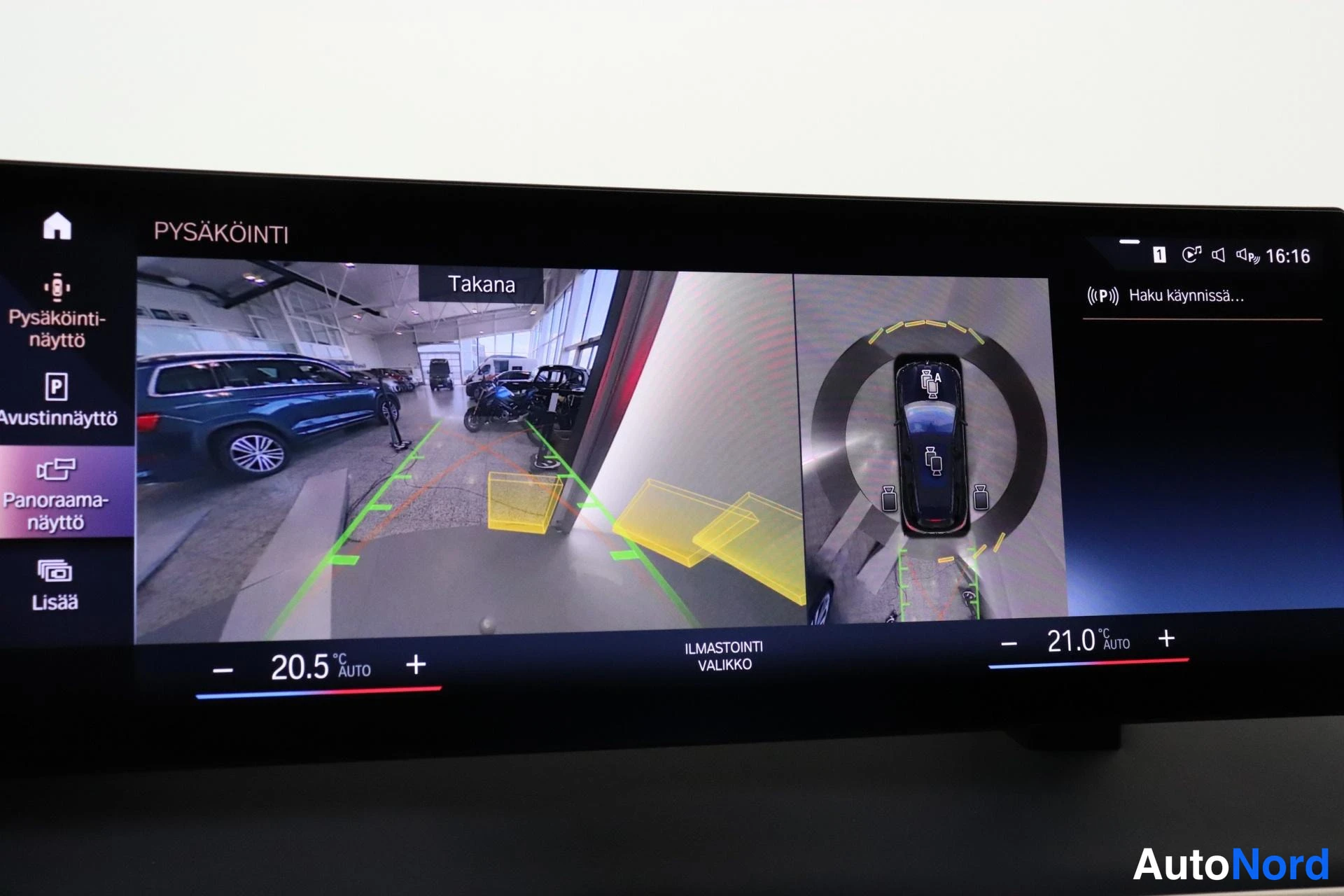 Ohjaamo: Oheinen kosketusnäyttö näyttää automaattisen pysäköintiavustin ja 360-kamerasovelluksen ruutua. Ruudulla on tekstiä 'Takana', 'PYSÄKÖINTI' ja 'Panoraamanäyttö'.