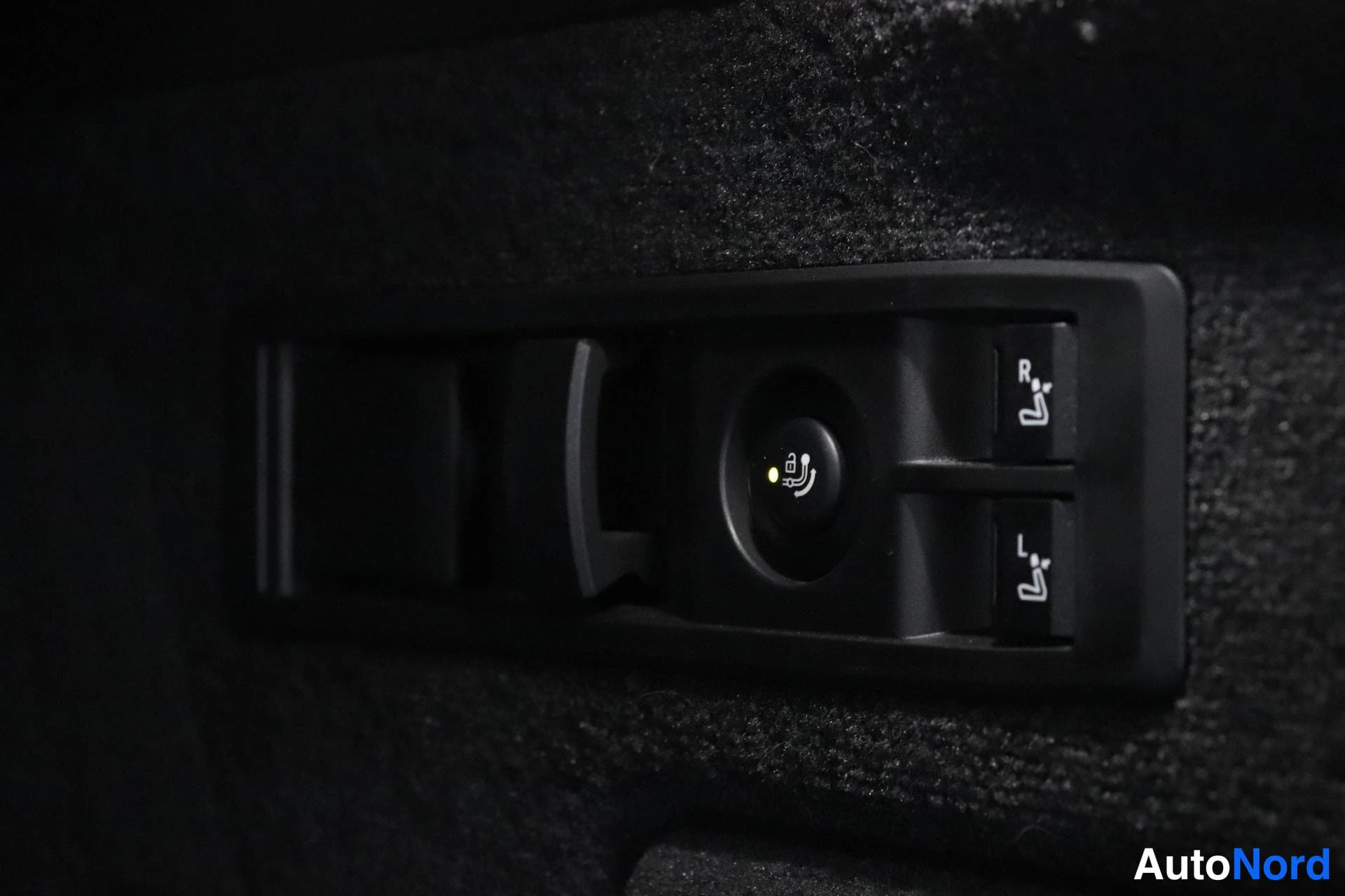 Yksityiskohta: Lähikuva mustasta paneelista tavaratilassa, jossa on kytkimet ISOFIX-kiinnityksien irrottamiseen. Paneelissa on R- ja L-merkitty painikkeenumerot sekä kesken va