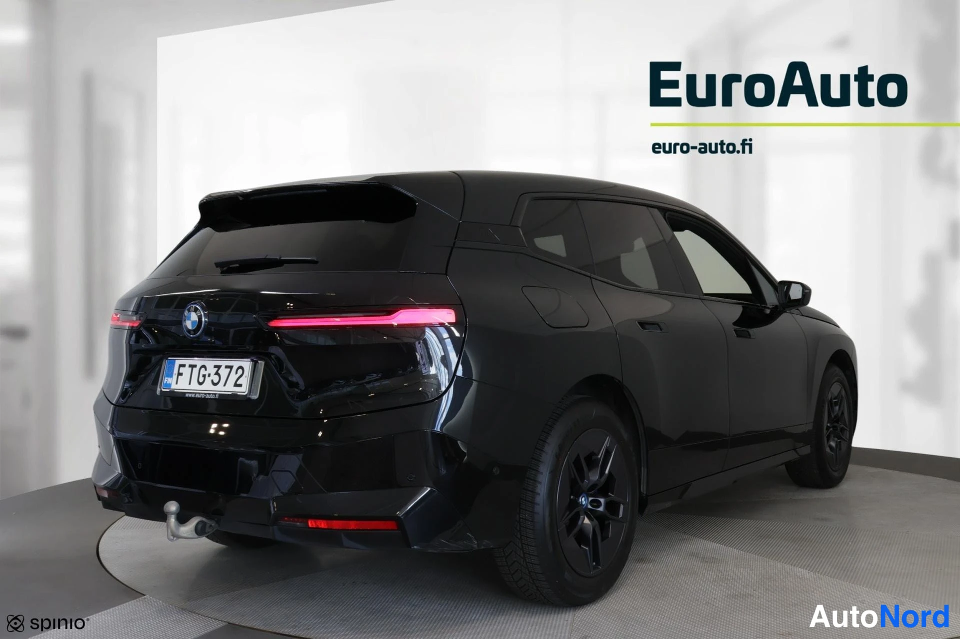 Takaviisto: Takaa vasemmalta kolmasosakuvana tummanharmaa BMW, jossa on kiinnitetty hinauspalkki. Etuvalot ja takavalot ovat päällä. Takalukko ja rekisteriluku näkyvät.