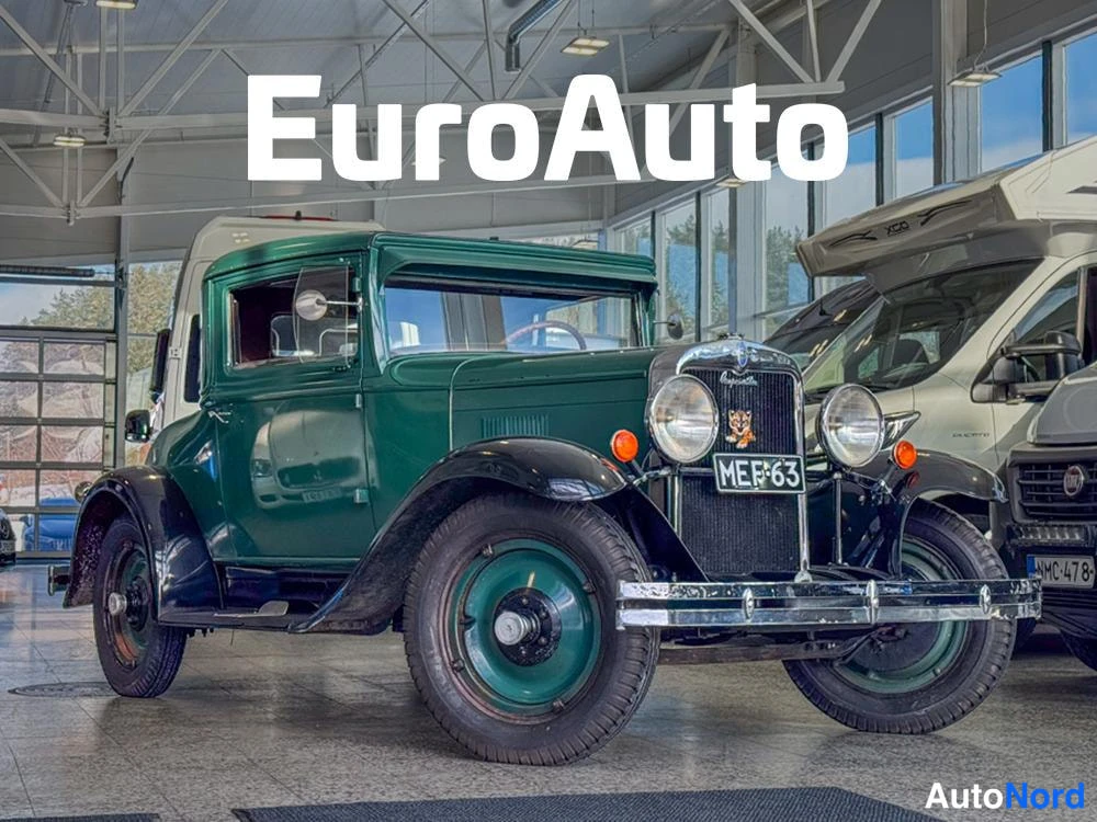 Etuviisto, nokka oikealle: Vihreä vintage-kupevaunu etukulmasta oikealta nähtynä: pyöreät ajovalot, kromattu etusäleikkö, rekisterikilpi ja mustat lokasuojat; kuvattu autonhallissa
