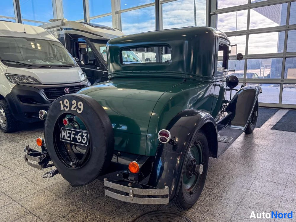 Takaviisto: Vihreä vintage-kupevaunu takakulmasta nähtynä toiselta sivulta: varapyörä tekstillä 1929, rekisterikilpi sekä perän ja oikean kyljen näkyessä lasiseinän edessä.