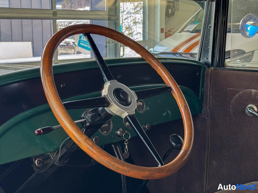 Yksityiskohta: Close-up detail of a large, thin-rimmed wooden steering wheel with chrome spokes and hub attached to a green dashboard panel.