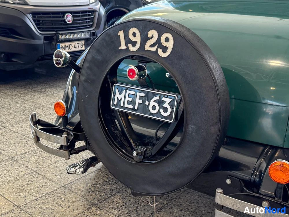 Takaviisto: Vähän vihreä auto takaa nähtynä. Takana on varren renkaaseen merkitty numero 1929. Autolla on tunnistusnumero.