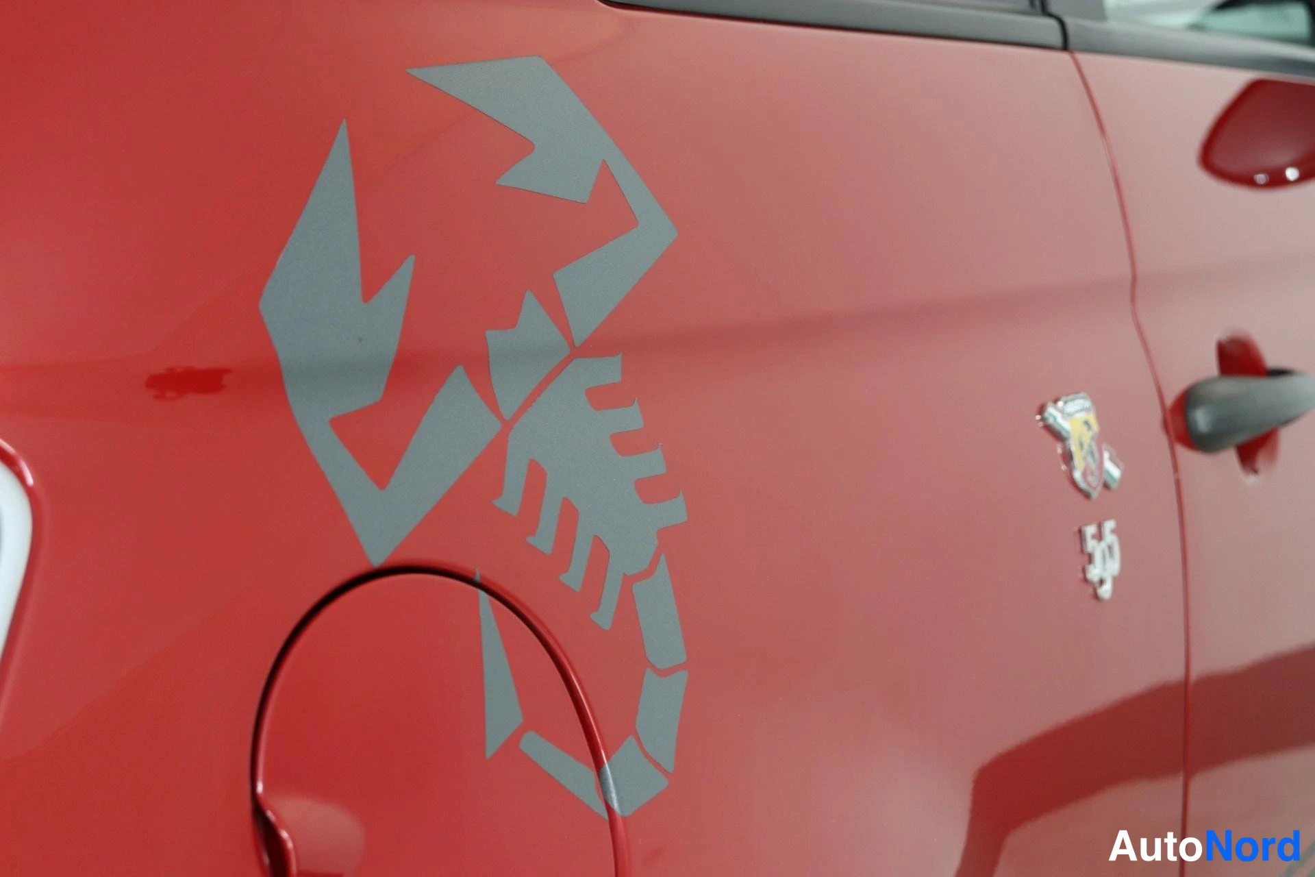 Yksityiskohta: Close-up detail of a grey scorpion decal on the rear quarter panel above the fuel filler cap. A silver scorpion badge and the number '595' are visible further f