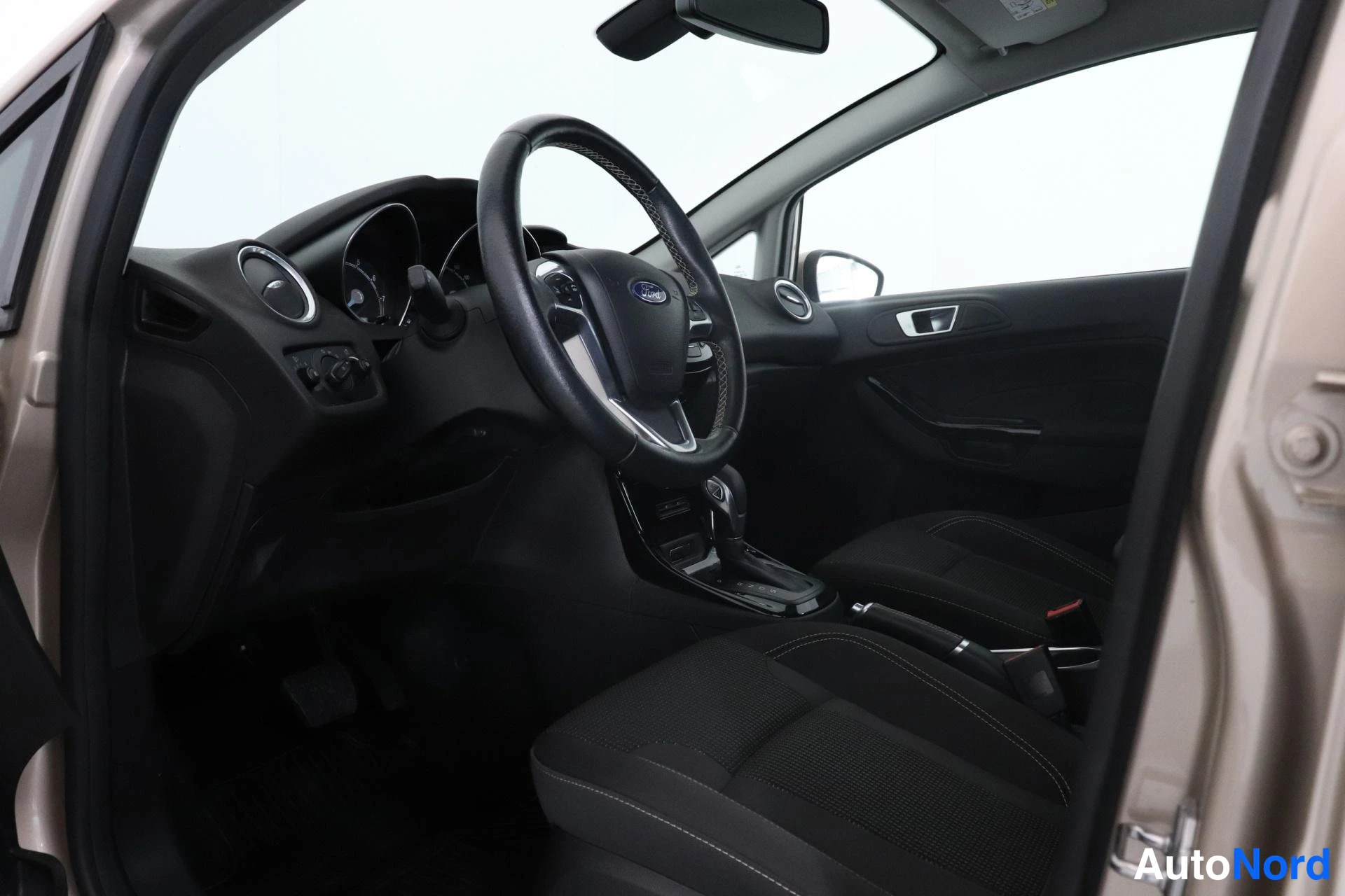 Ohjaamo: Interior view of the front cabin showing black fabric driver and front passenger seats, multifunction steering wheel and central console.