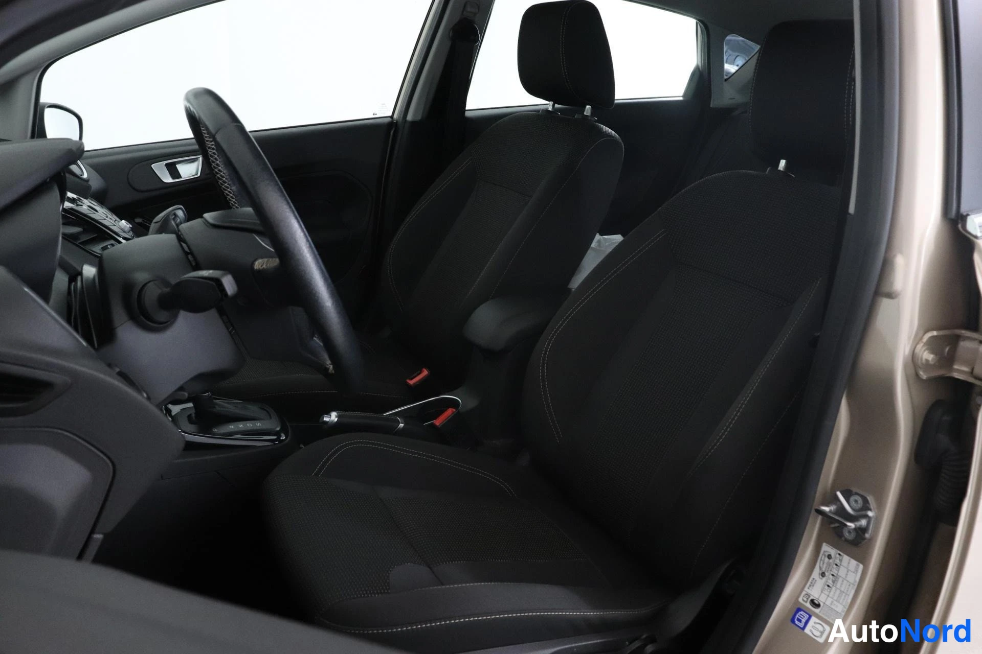 Etuistuimet: Front seats and dashboard area viewed through the open passenger door; two front bucket seats visible in dark fabric with stitching.