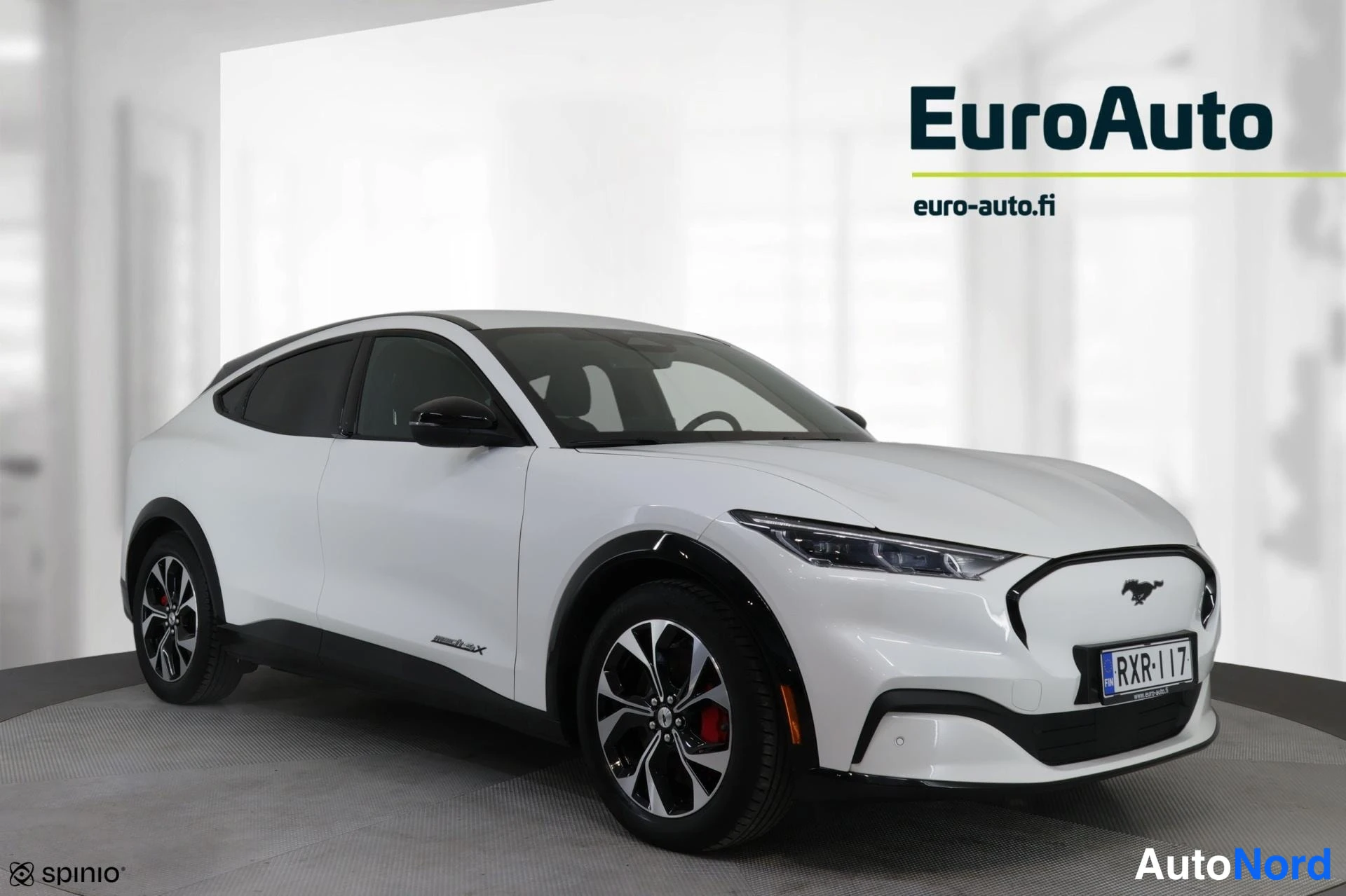 Etuviisto, nokka oikealle: Valkoinen Ford Mustang Mach-E etuviistokuva, keula kuvan oikealla; musta katto, kevytmetallivanteet ja rekisteritunnus.