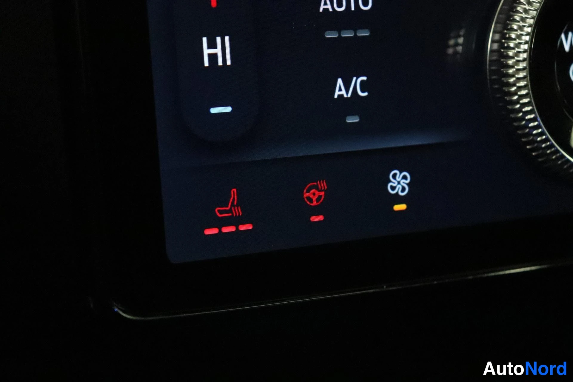 Muu: Ilmastoinnin kosketusnäytön lähikuva: A/C, AUTO ja HI sekä punaiset kuvakkeet istuin- ja ohjauspyöränlämmitykselle.