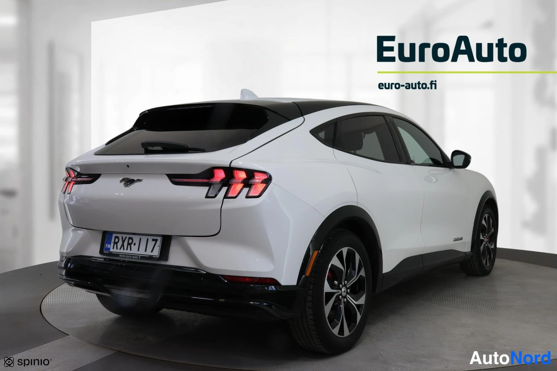 Takaviisto: Valkoinen Ford Mustang Mach-E takaviistokuva, perä kuvan vasemmalla; kolmiosaiset takavalot, musta lasikatto ja rekisteritunnus.
