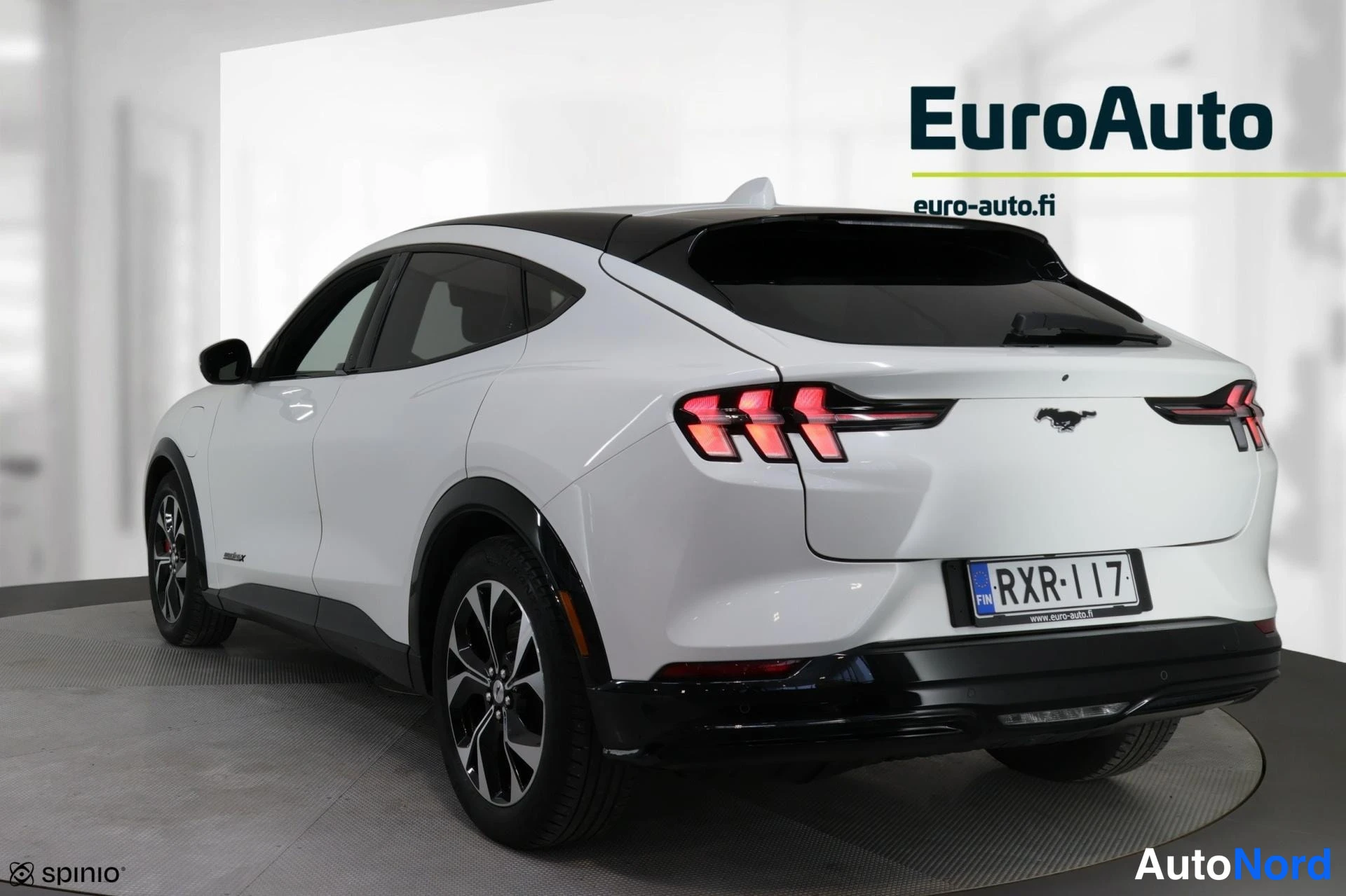 Takaviisto: Valkoinen Ford Mustang Mach-E takaviistokuva, perä kuvan oikealla; kylki ja takavalot näkyvissä, rekisteritunnus.