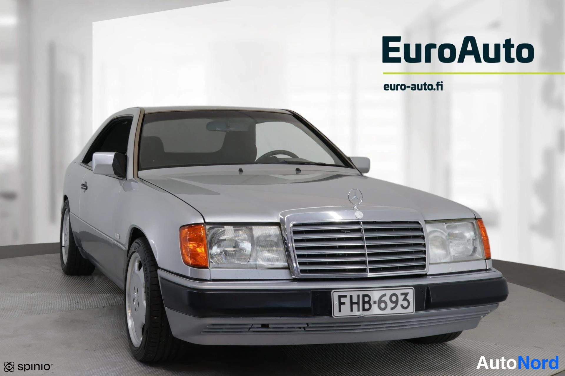 Etuviisto, nokka oikealle: Hopeanharmaa Mercedes-Benz-coupé kuvattuna etuviistosta studiotaustaa vasten; keula oikealla, kylki näkyy vasemmalla. Etusäleikkö tähtimerkillä, ajovalot