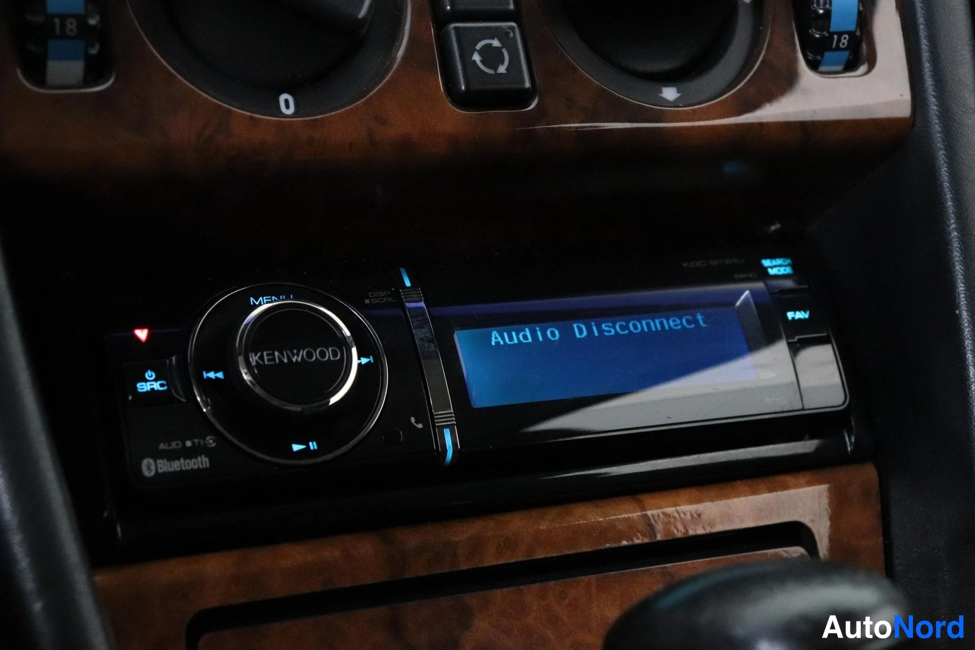 Muu: Kenwood-autoradio kojelaudassa, näytöllä teksti 'Audio Disconnect'; ympärillä puusisustaa ja ilmastoinnin säätimiä.