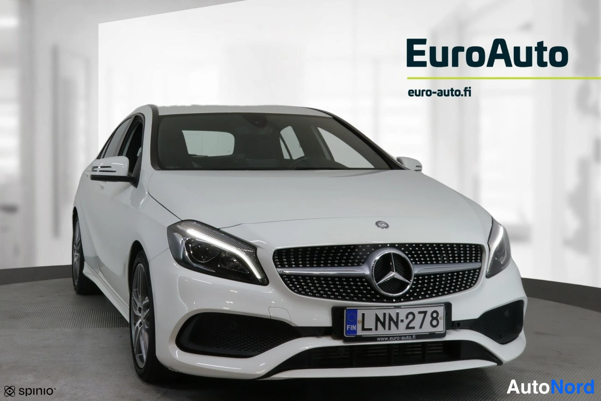 Etuviisto, nokka vasemmalle: Valkoinen Mercedes-Benz -henkilöauto etuviistokuvassa valkoisessa tilassa. Auton keulapaneeli, grilli ja vasen sivu näkyvät.
