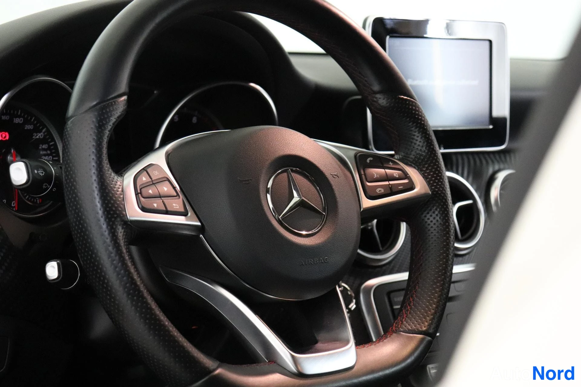 Etuviisto: Sisätilan lähikuva Mercedes-ohjauspyörästä: tähtimerkki ja AIRBAG-teksti ohjauspyörän napissa, monitoiminapit puolissa, taustalla kojetaulin mittaristo, erillin