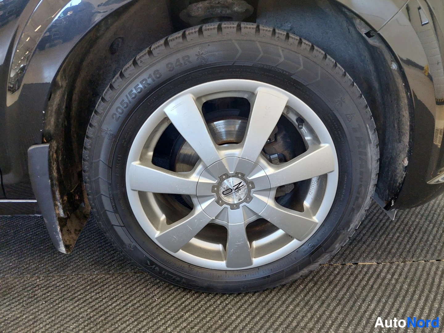 Sivulta: Auton pyörä lähikuvassa: hopeavanne, kitkarengas, sivumerkintä 205/55R16 94R.