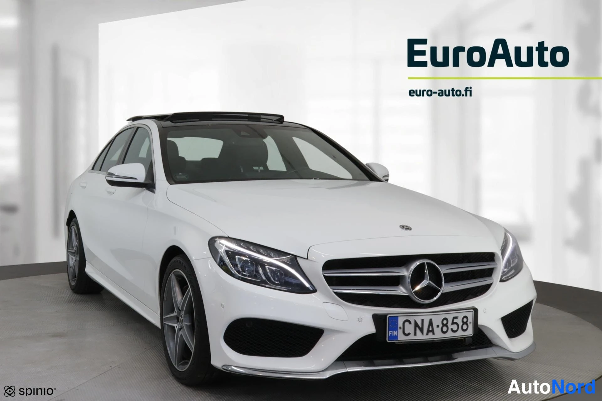 Etuviisto, nokka oikealle: Valkoinen Mercedes-Benz-sedan lähes suoraan edestä, vasen kylki osittain kuvassa; lasikatto, kevytmetallivelimet ja rekisterikilpi näkyvissä.