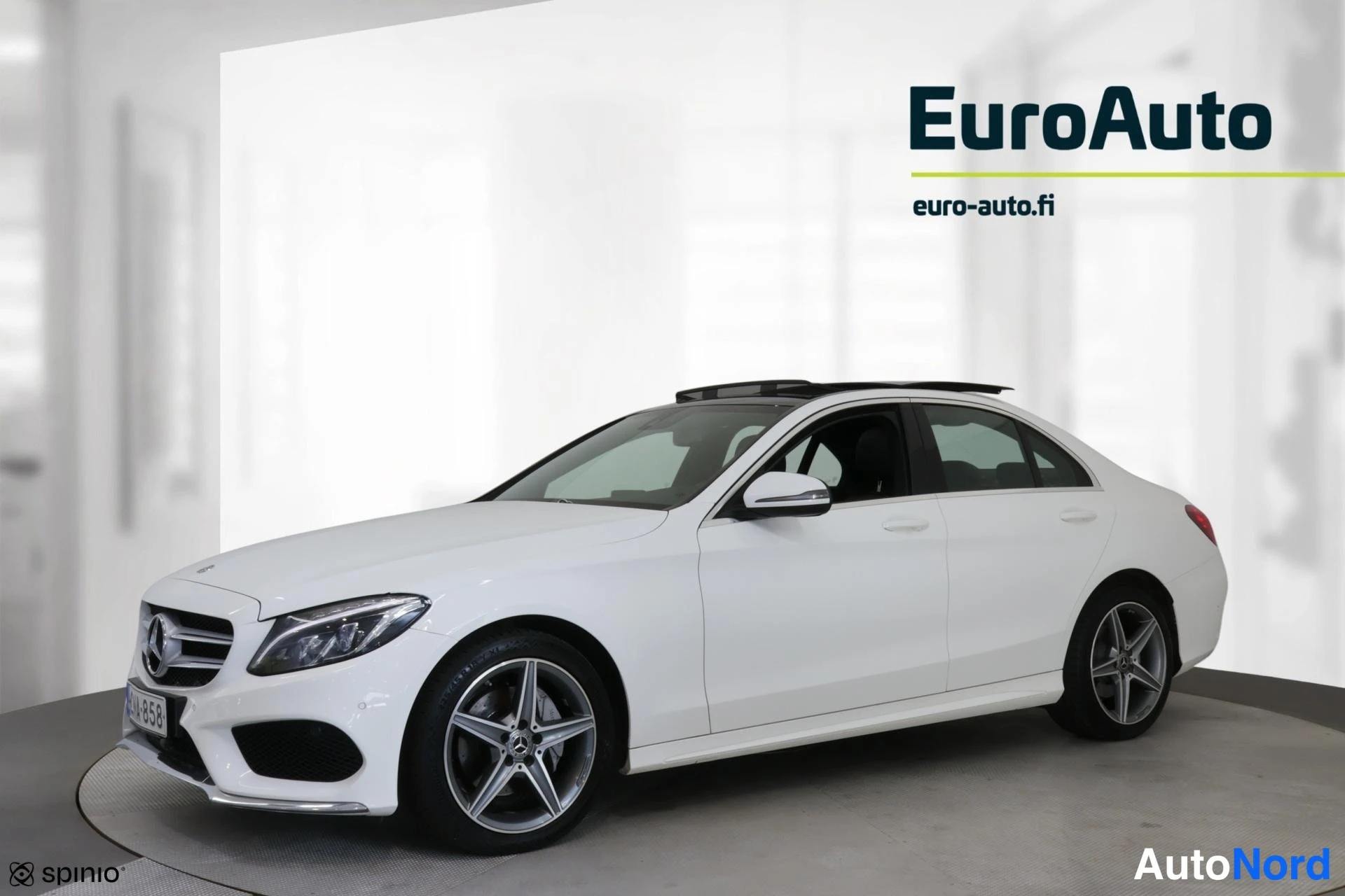 Etuviisto, nokka vasemmalle: Valkoinen Mercedes-Benz-sedan etuviistosta, keula kuvan vasemmassa laidassa; lasikatto, kevytmetallivelimet ja rekisterikilpi näkyvissä.