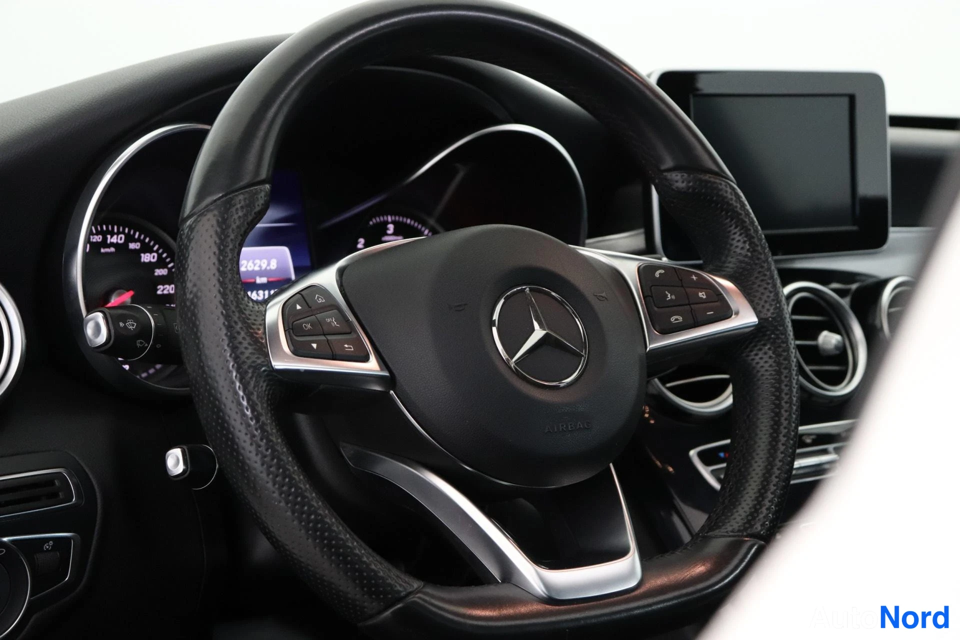 Ohjaamo: Close-up of the leather-wrapped multifunction steering wheel with Mercedes-Benz logo; instrument cluster visible behind showing odometer reading and infotainmen